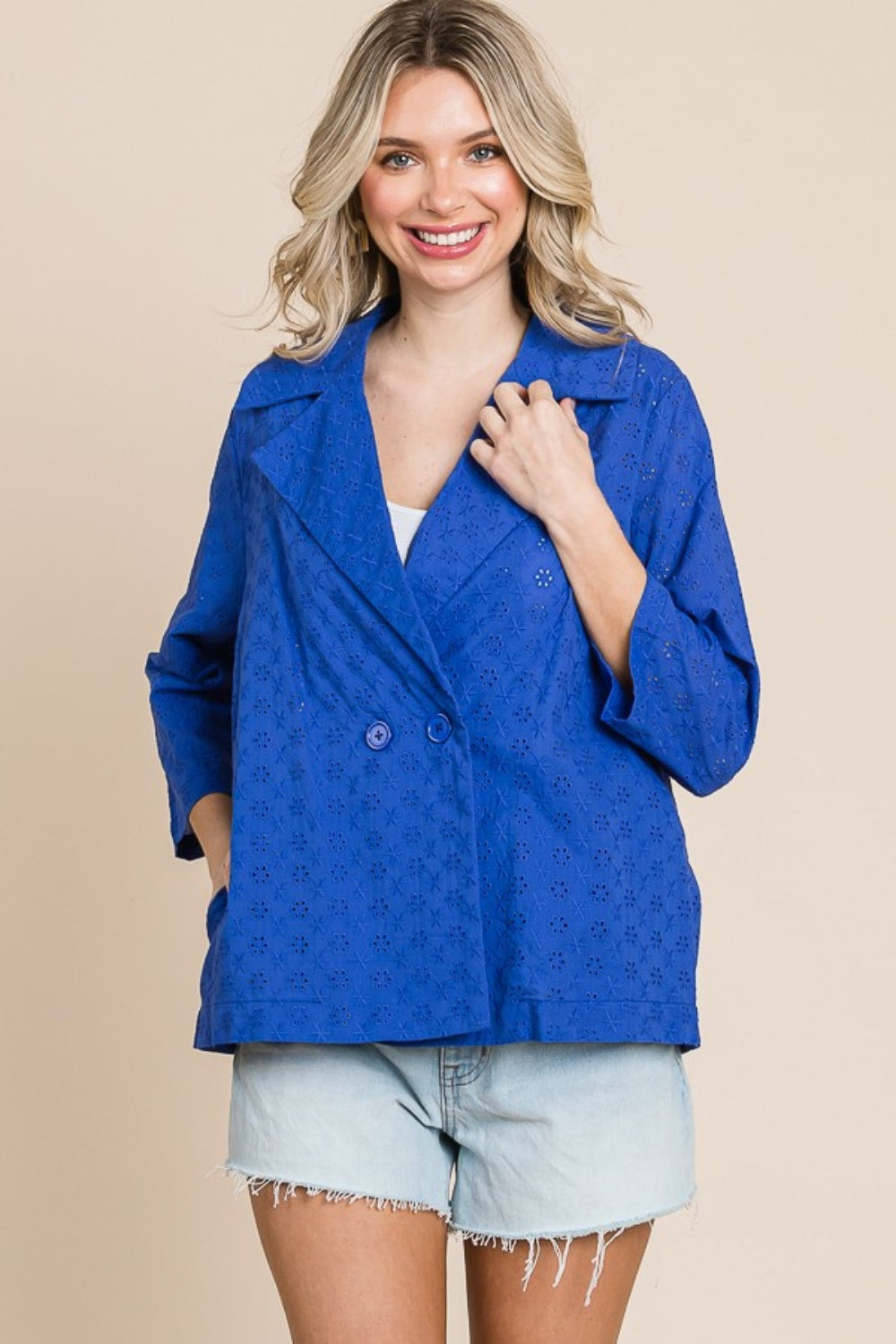 Person smiling, wearing a Culture Code Double Breasted Eyelet Jacket with Pockets over a white top and denim shorts, holding a small textured handbag.