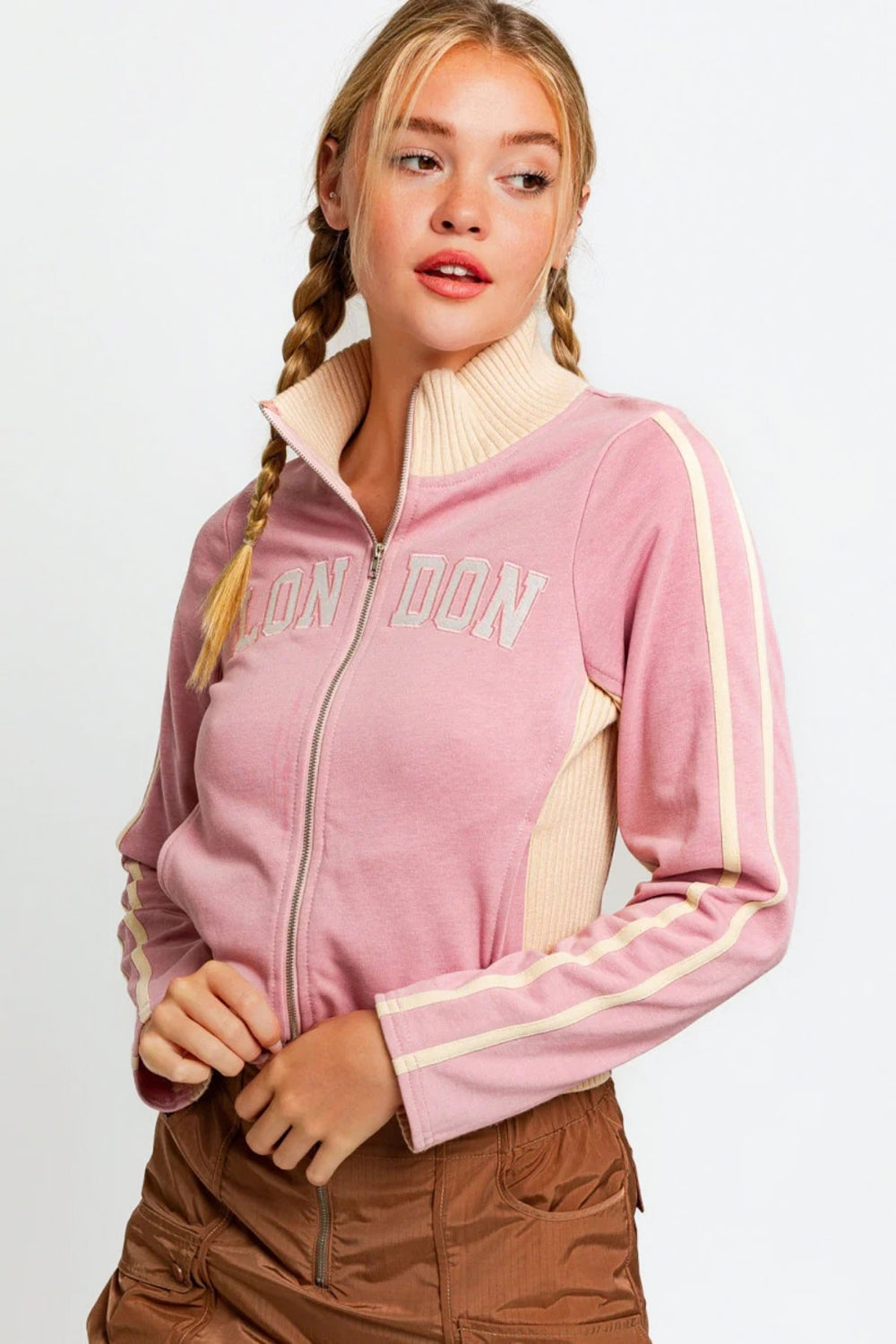 A person wearing the Le Lis Long Sleeve Mock Neck LONDON Embroidered Jacket in light pink and brown pants, looking to the side.