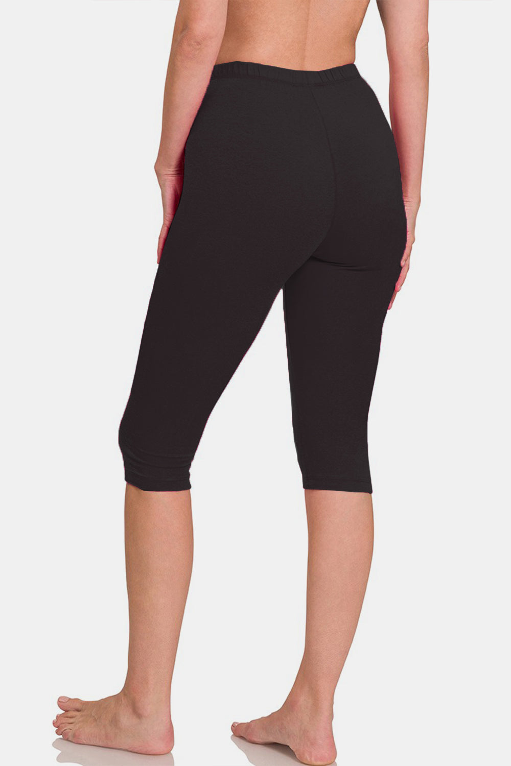 A person is standing barefoot wearing Zenana Full Size High Waist Capris, black knee-length leggings with a flattering fit, against a plain white background.