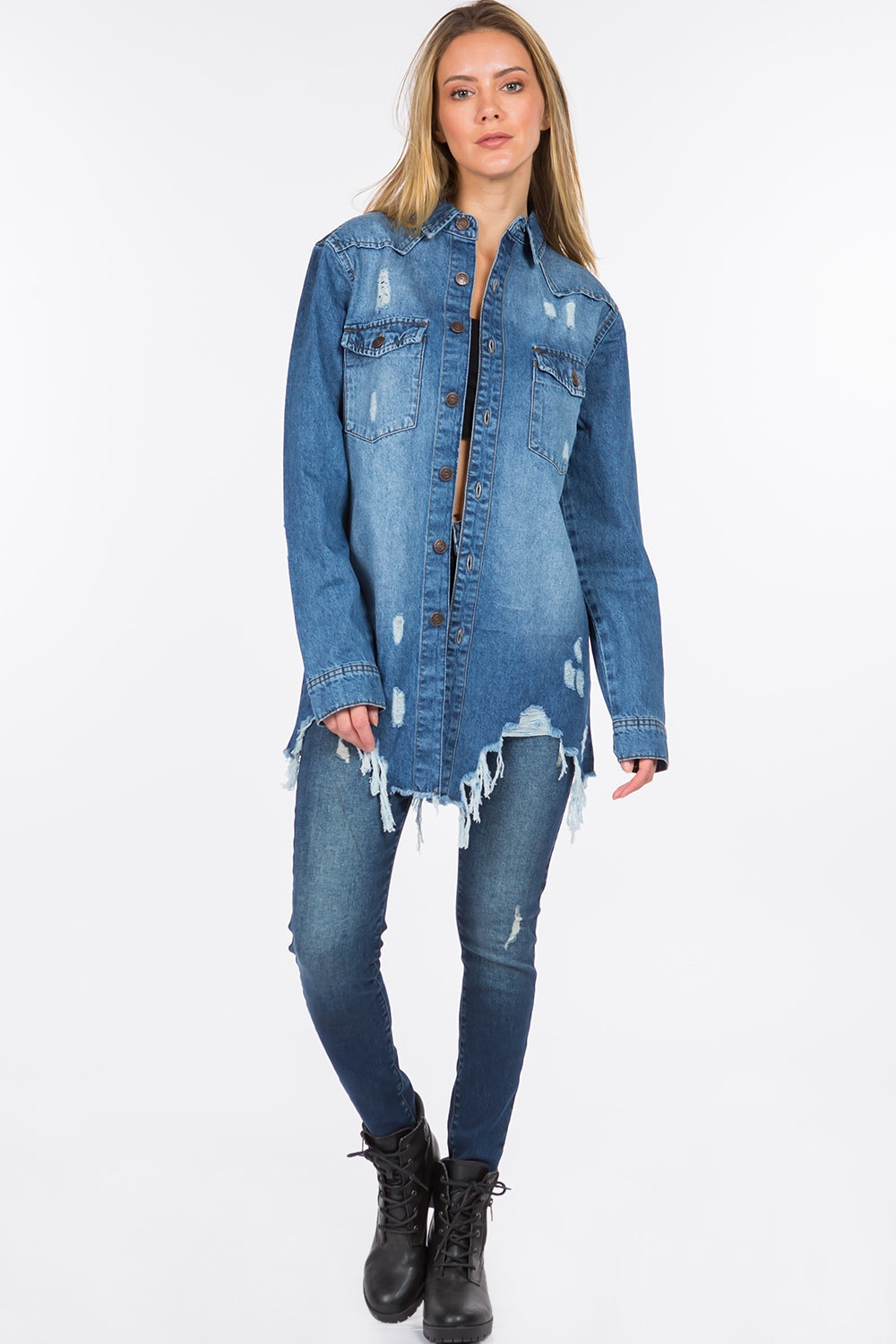 A person with long hair is standing, wearing an American Bazi Distressed Frayed Hem Denim Jacket over a black top and denim jeans with a frayed hem.