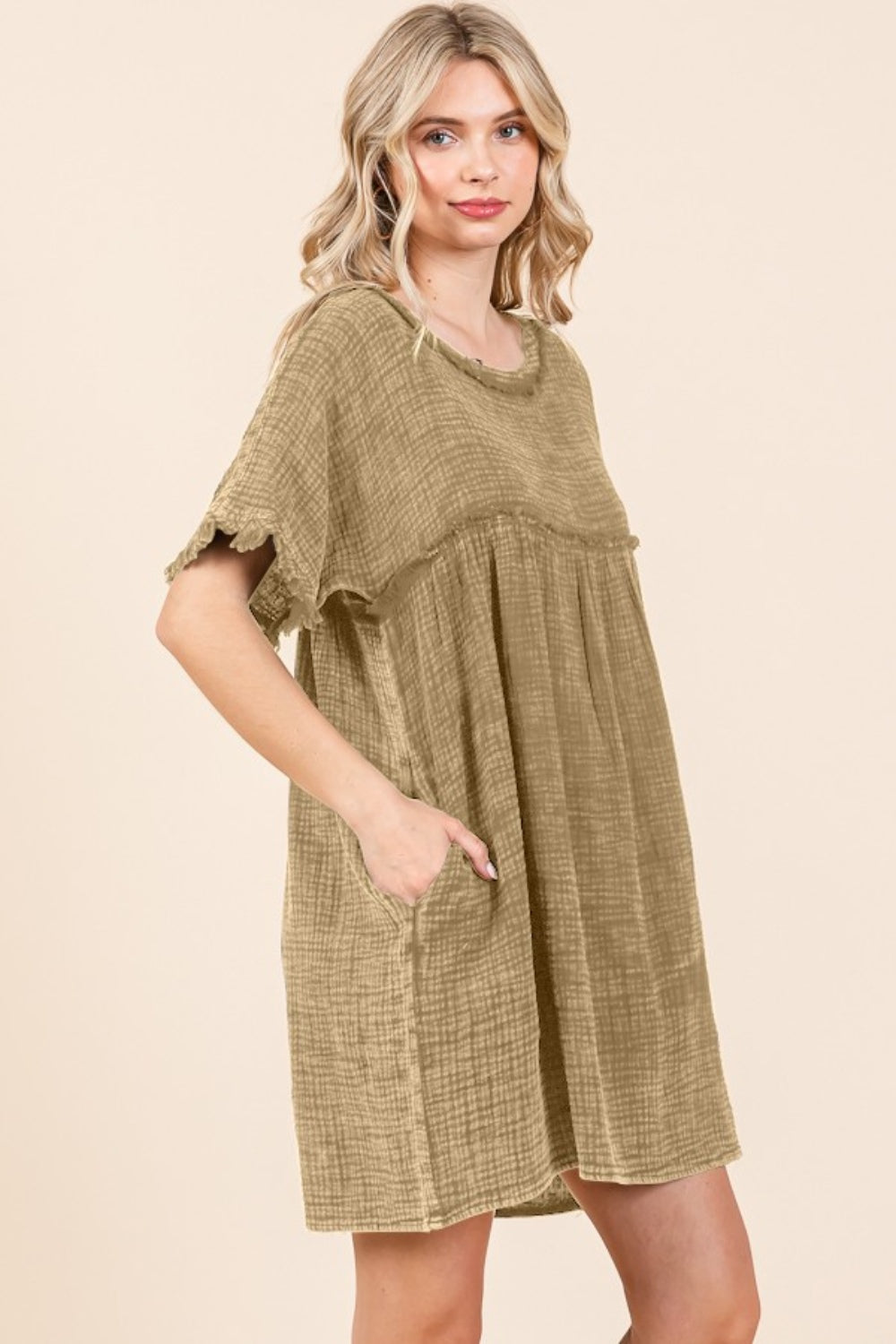 A person is wearing the Culture Code Full Size Short Sleeve Babydoll Texture Dress with Pockets, characterized by its loose fit and short sleeves, in a light brown shade, while standing against a plain background.