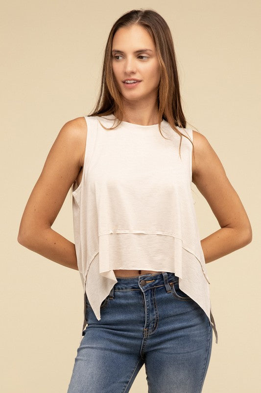 Wearing the Shark Bite Side Slit Short Sleeveless Top in maroon paired with white pants, a model is set against a beige background, exemplifying an effortlessly chic and casual wardrobe.