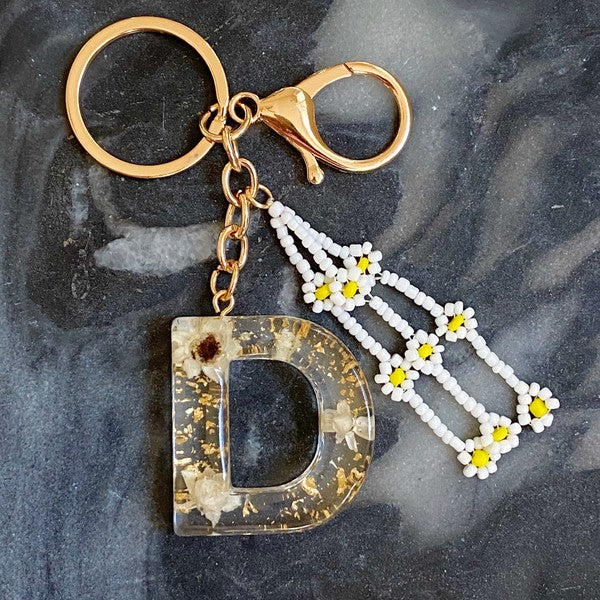 Baby Daisy Initial Key Chain alphabet keychains with real daisy flowers and gold flakes on a marble surface.