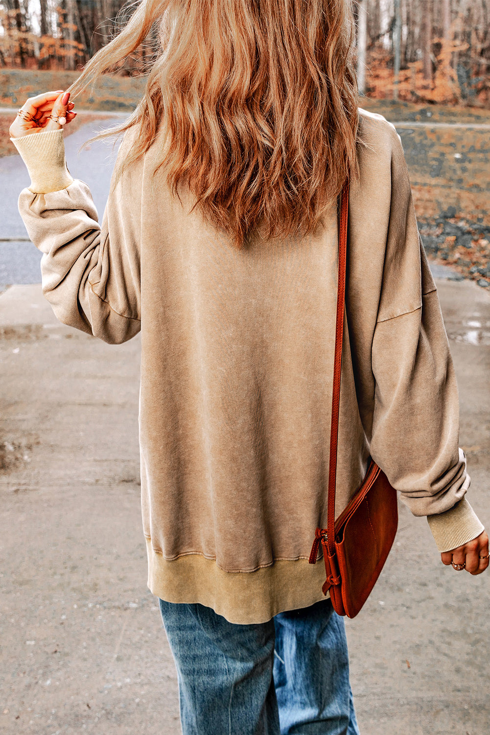 Person with wavy blonde hair wearing a Khaki Drop Shoulder Ribbed Trim Oversized Sweatshirt and blue jeans, walking outdoors with a brown leather crossbody bag.