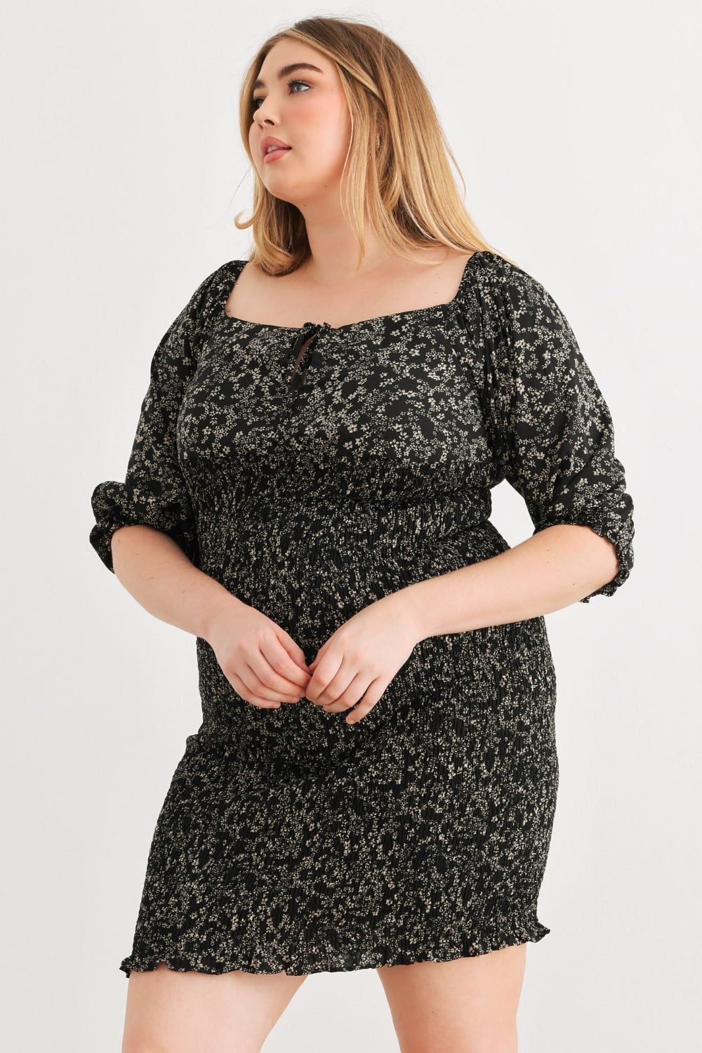 A person poses confidently wearing the Zenobia Plus Size Smocked Printed Square Neck Mini Dress in black and white, paired with black sandals, against a plain white background.