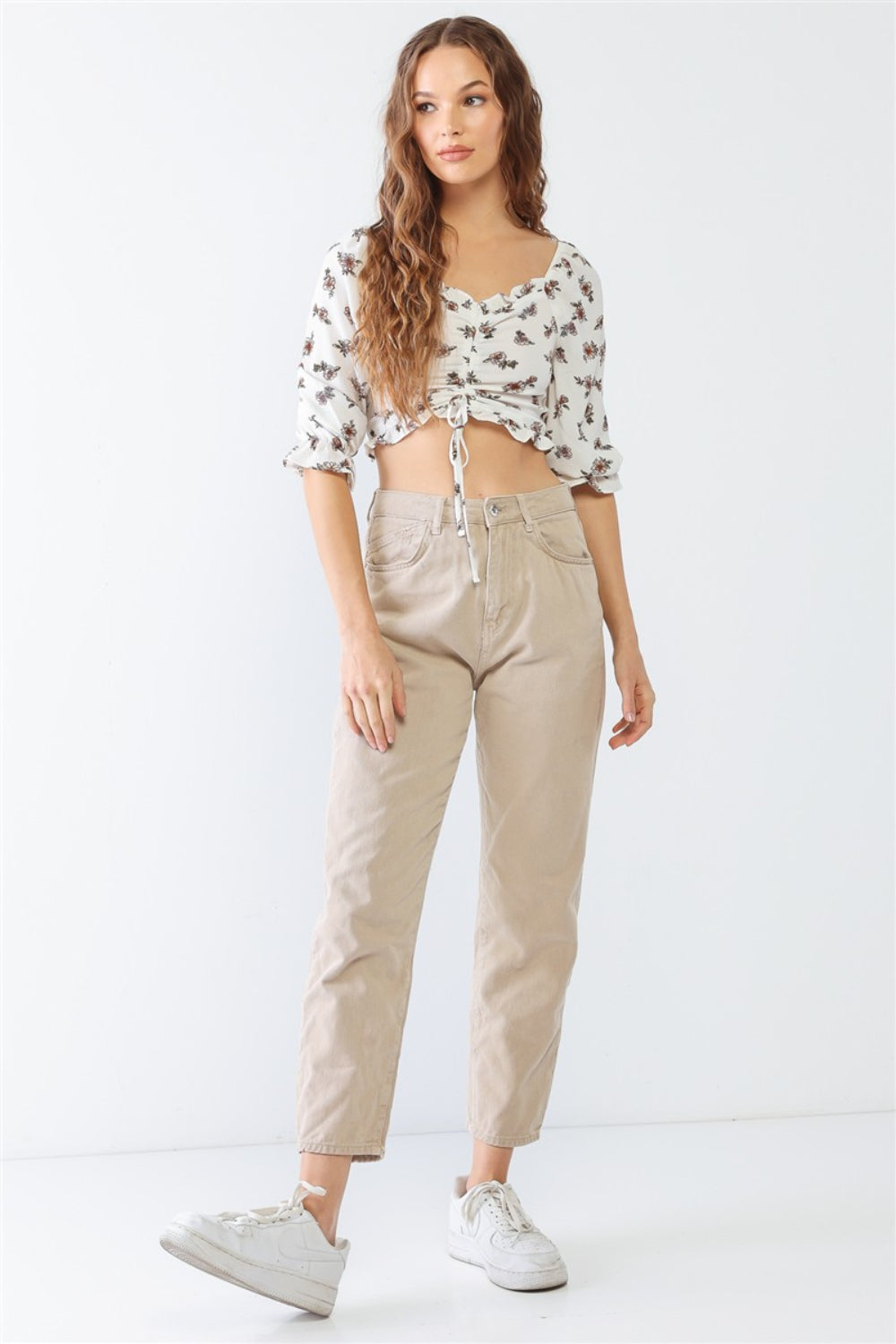 A woman with long hair poses in the PAPERMOON Floral Ruffled Smocked Crop Top, elegantly paired with light beige pants against a plain background.