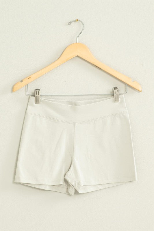 The Take Pride Mid-Rise Biker Shorts, crafted from stretch fabric, hang gracefully on a wooden hanger against a pale wall.