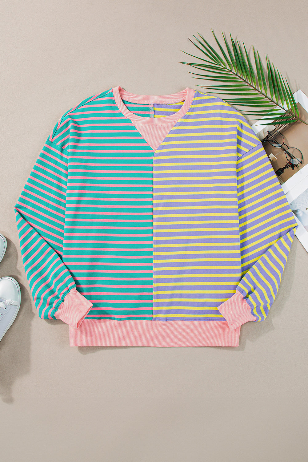 A person with wavy hair is seen from behind wearing a Casual Stripe Colorblock Drop Shoulder Oversize Sweatshirt in pastel colors and blue jeans. They are carrying a white shoulder bag, showcasing a trendy color block design.