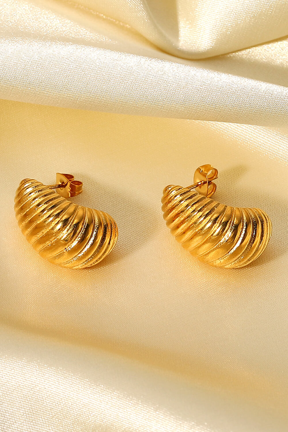 A pair of Shell Shore Spiral Stud Earrings, gold-plated with a ribbed, crescent shape and post-butterfly clasps on a white background.