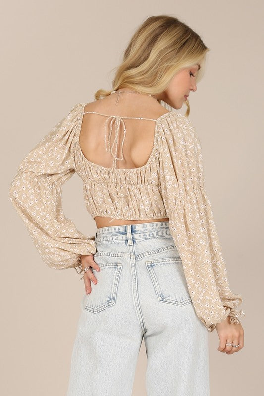 A person wearing an LS square neck floral crop top paired with light blue jeans poses against a beige background.