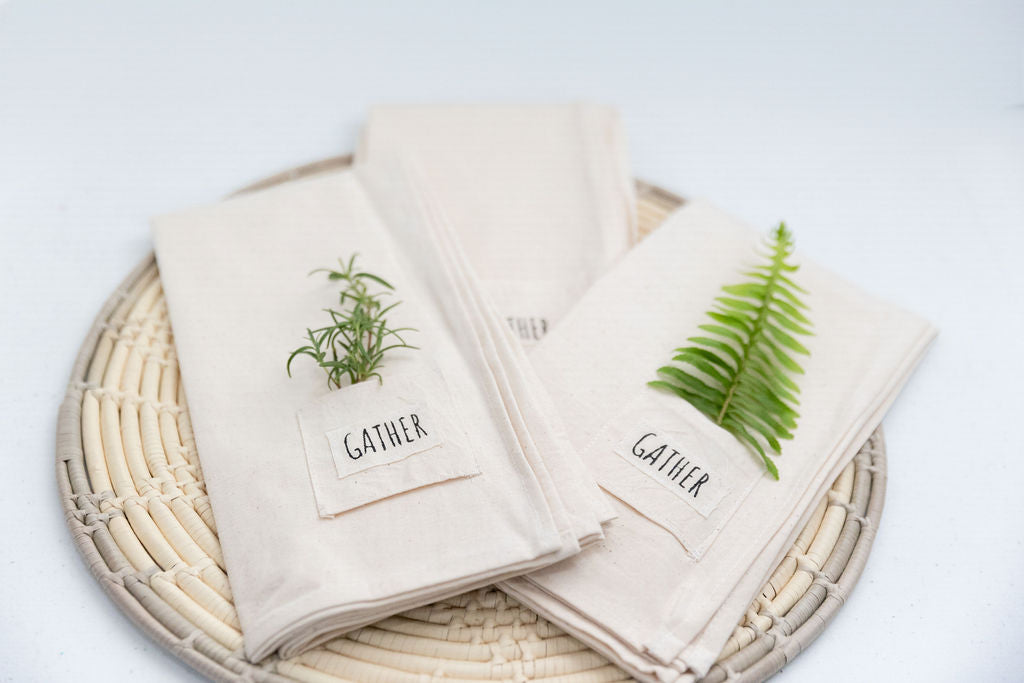 Pocket napkin set of four, skillfully crafted from up-cycled fabric, folded with a eucalyptus sprig and wooden ring, labeled "SAVOR.