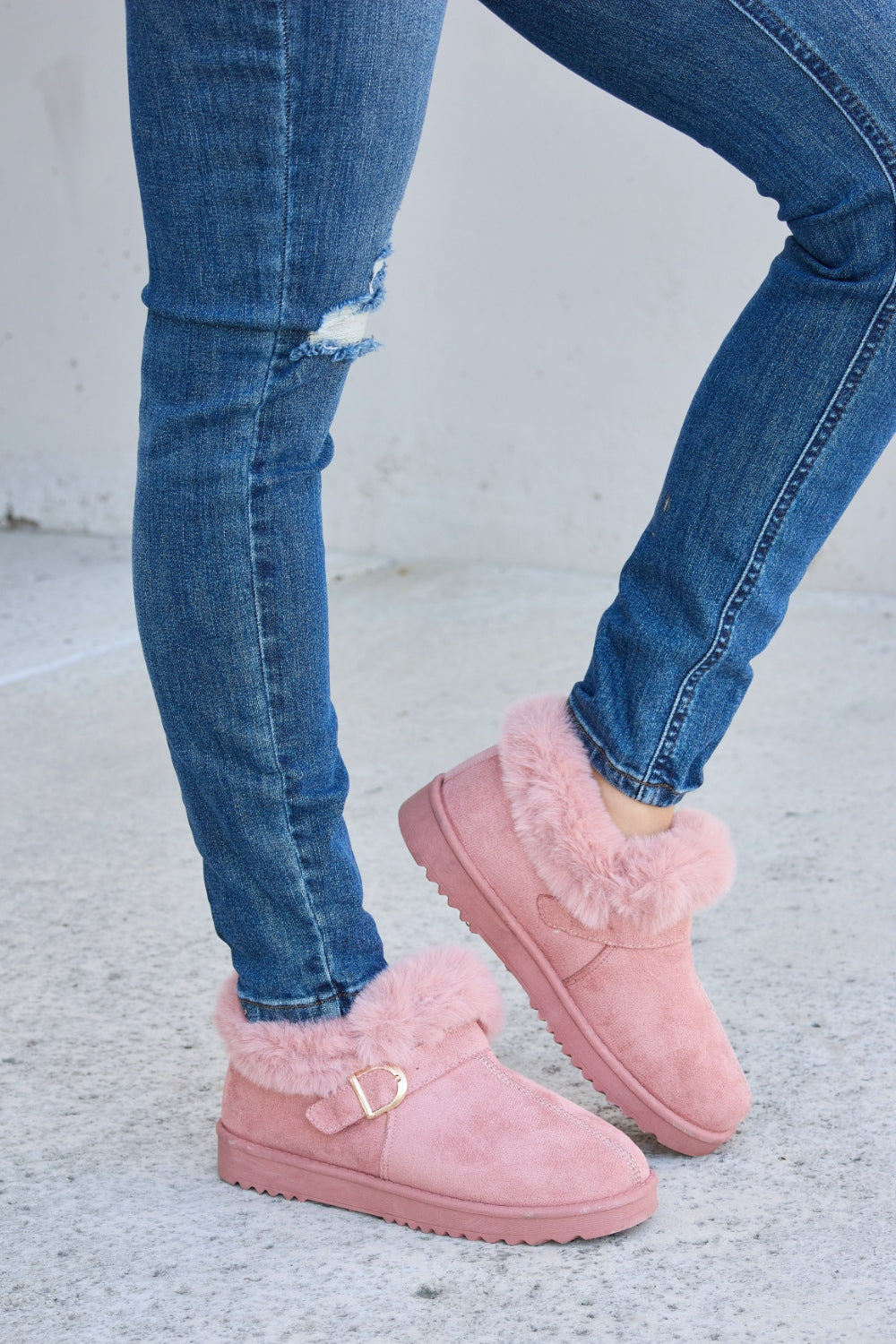 A person stands on a concrete surface, sporting ripped blue jeans and the Forever Link Furry Chunky Thermal Ankle Boots. The furry lining of these fashionable boots suggests both comfort and warmth for winter.