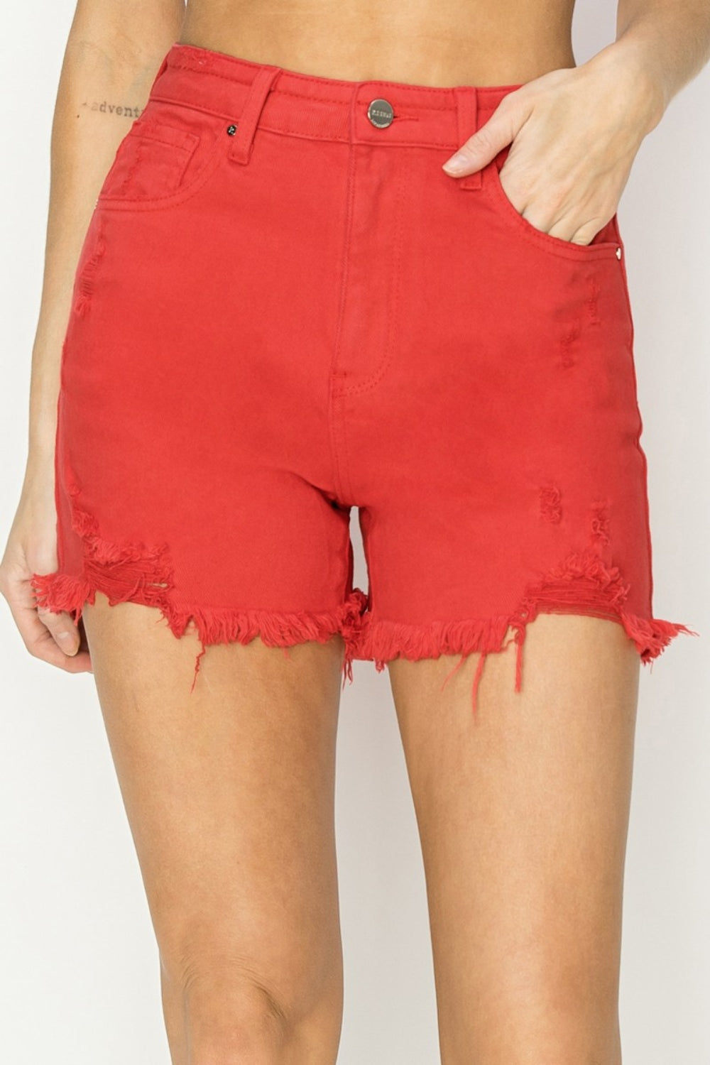 Close-up of a person wearing trendy RISEN High Rise Distressed Denim Shorts with distressed hems and pockets. The versatile wardrobe essential shorts feature a button and zip closure.