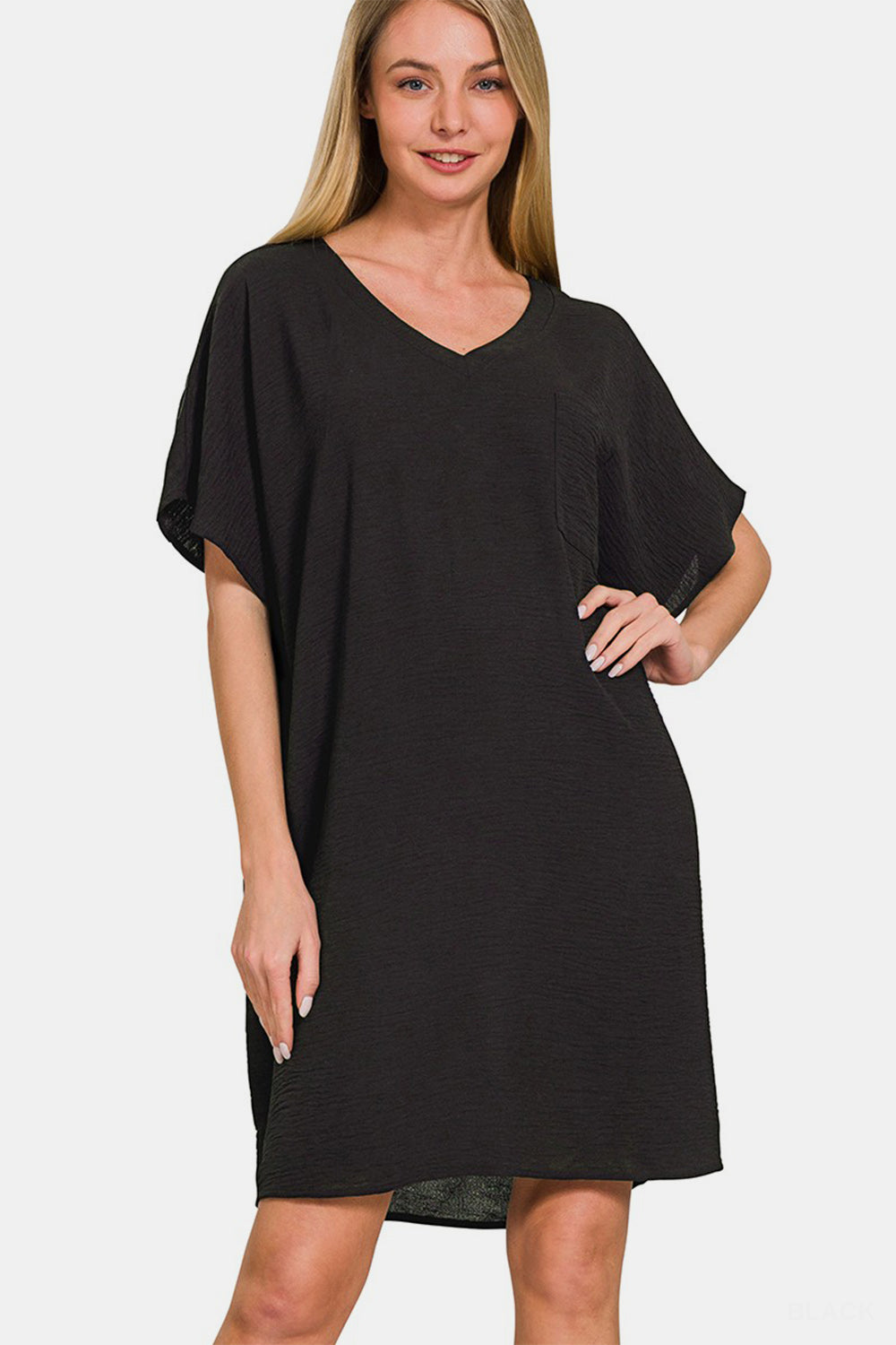 A woman with long hair is sporting the Zenana V-Neck Tee Dress with Pockets, a comfortable, loose-fitting black dress featuring short sleeves. She is smiling and has one hand on her hip.