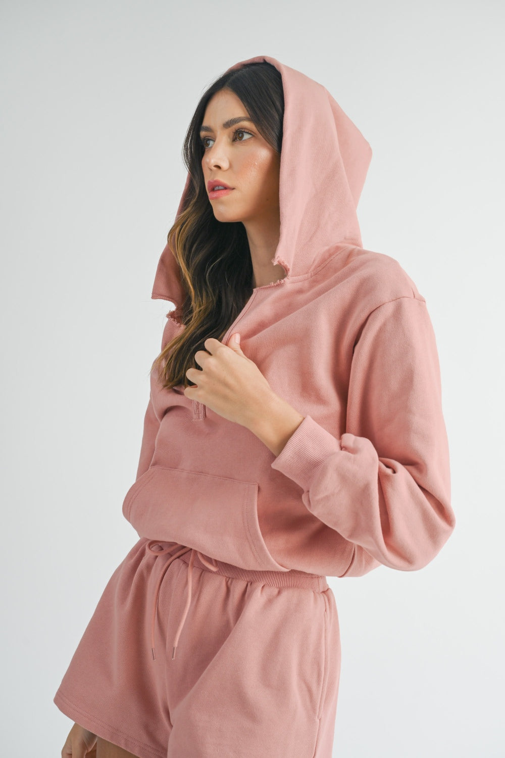 Woman wearing a MABLE French Terry Hooded Romper in pink, hands in pockets, looking directly at the camera.