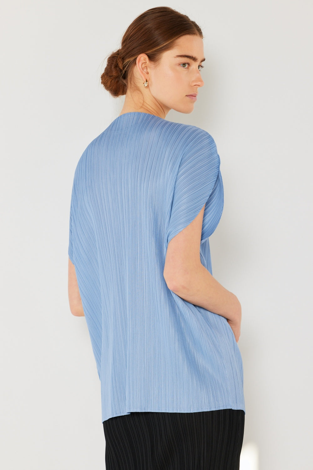 A person wearing the Marina West Swim Rib Pleated Oversized Dolman Sleeve Top in a fashionable light blue shade, paired with a brown belt and black skirt, stands against a plain background.