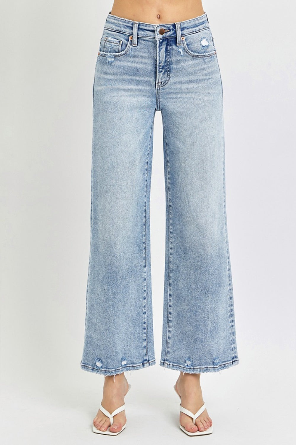 A person wearing RISEN Full Size Tummy Control High Rise Crop Wide Leg Jeans in a light-wash with a frayed hem and white open-toe sandals.