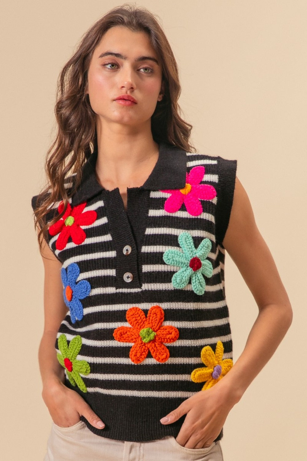 A person wearing the BiBi Flower Patch Striped Half Button Sweater Vest, a sleeveless top featuring black and white stripes adorned with colorful floral patches.