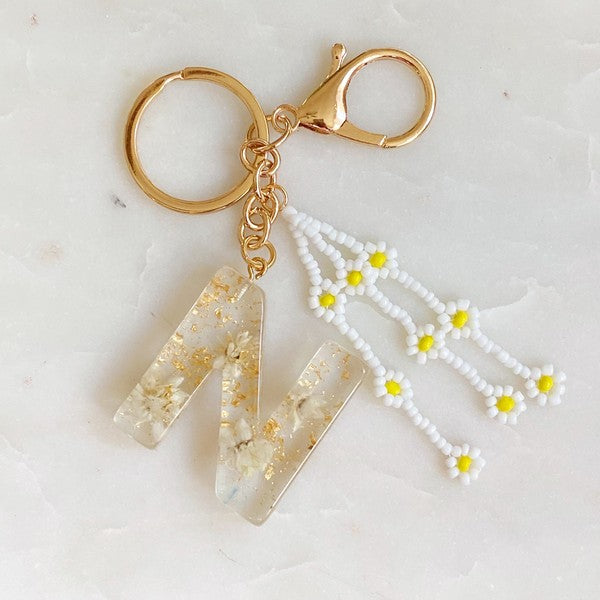 Baby Daisy Initial Key Chain alphabet keychains with real daisy flowers and gold flakes on a marble surface.