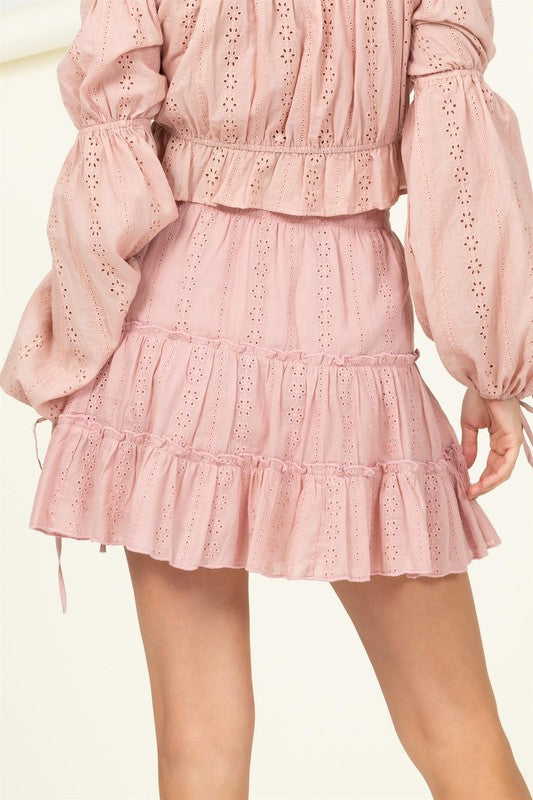 A person wearing the Forever Classy High Waist Tiered Mini Skirt in pink, featuring eyelet details and a ruffled design.