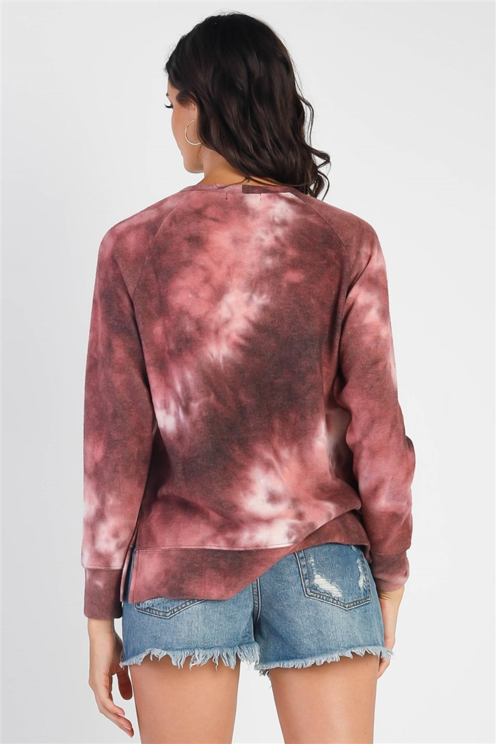 A person wearing the Cherish Apparel Tie-Dye Round Neck Long Sleeve Sweatshirt and distressed denim shorts stands against a plain background, showcasing effortless casual fashion.