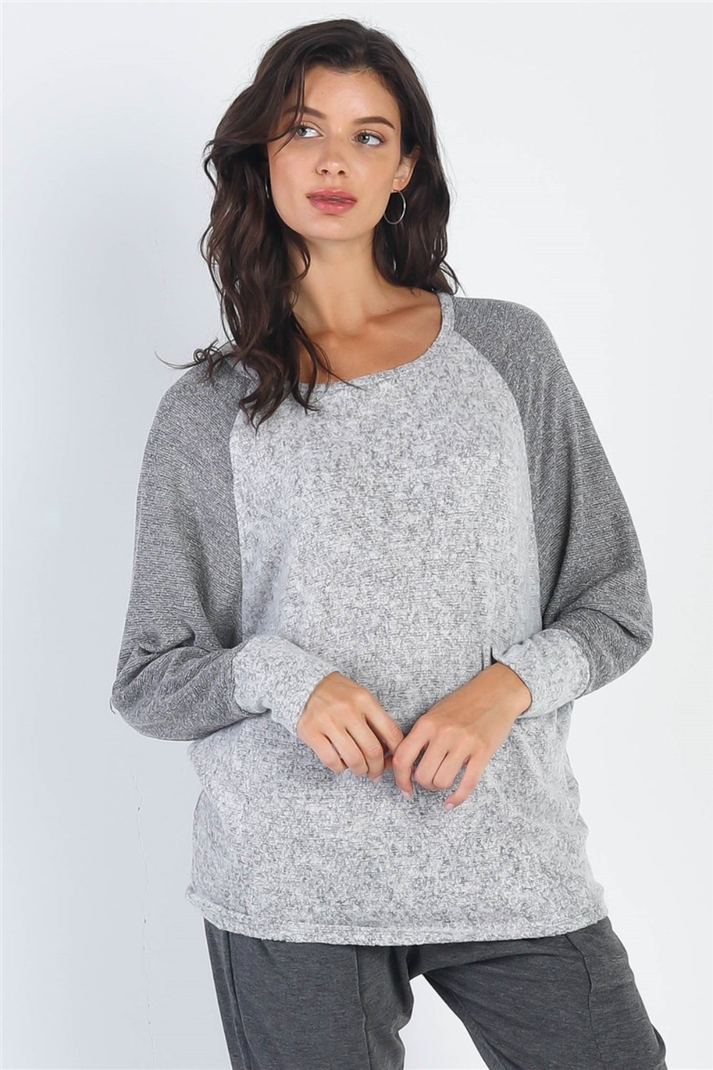 A woman stands wearing the Cherish Apparel Round Neck Long Sleeve Contrast Top in pink and gray with matching gray pants, set against a plain background.