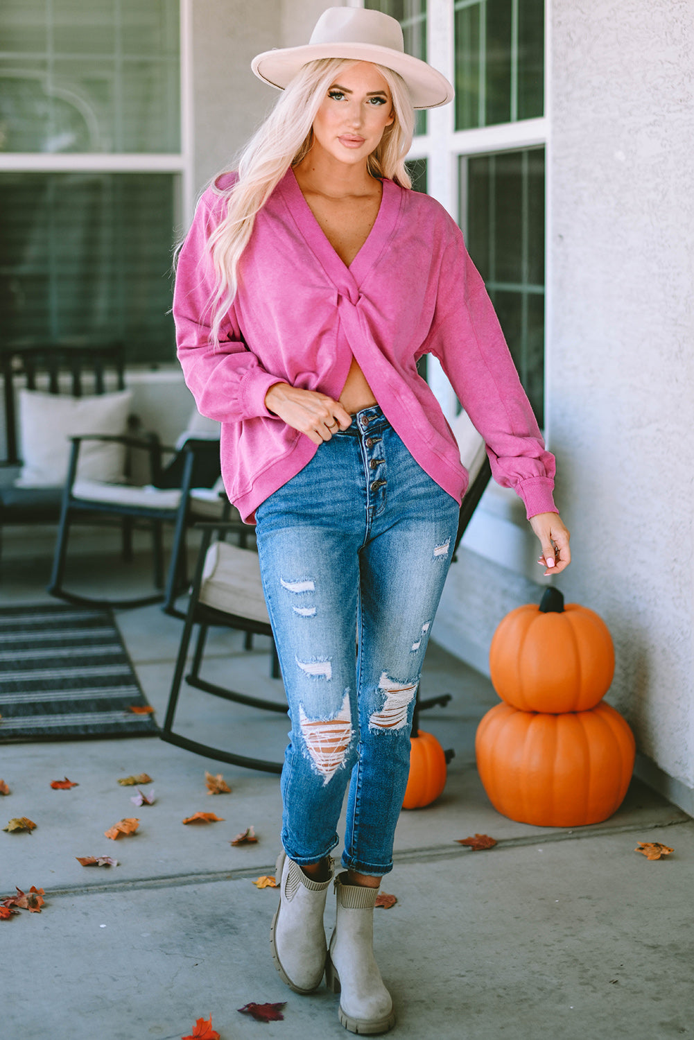 A woman stands with her back to the camera, wearing a long-sleeved Rose Exposed Seam Twist Open Back Oversized Sweatshirt and light blue jeans, showcasing a relaxed fit.