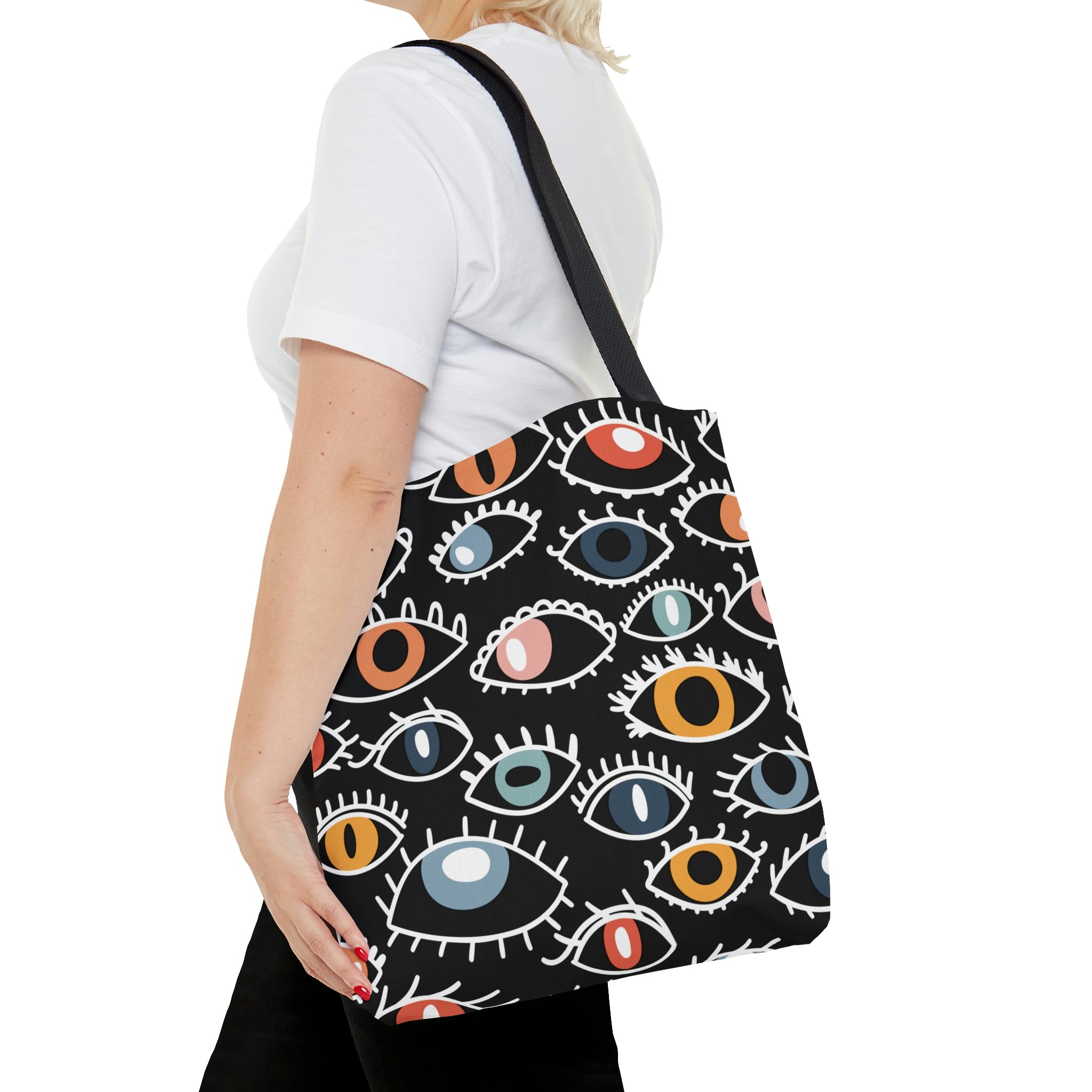 A shopping tote bag featuring a pattern of stylized Egyptian eyes in various colors and designs on a black background, complete with black cotton handles.