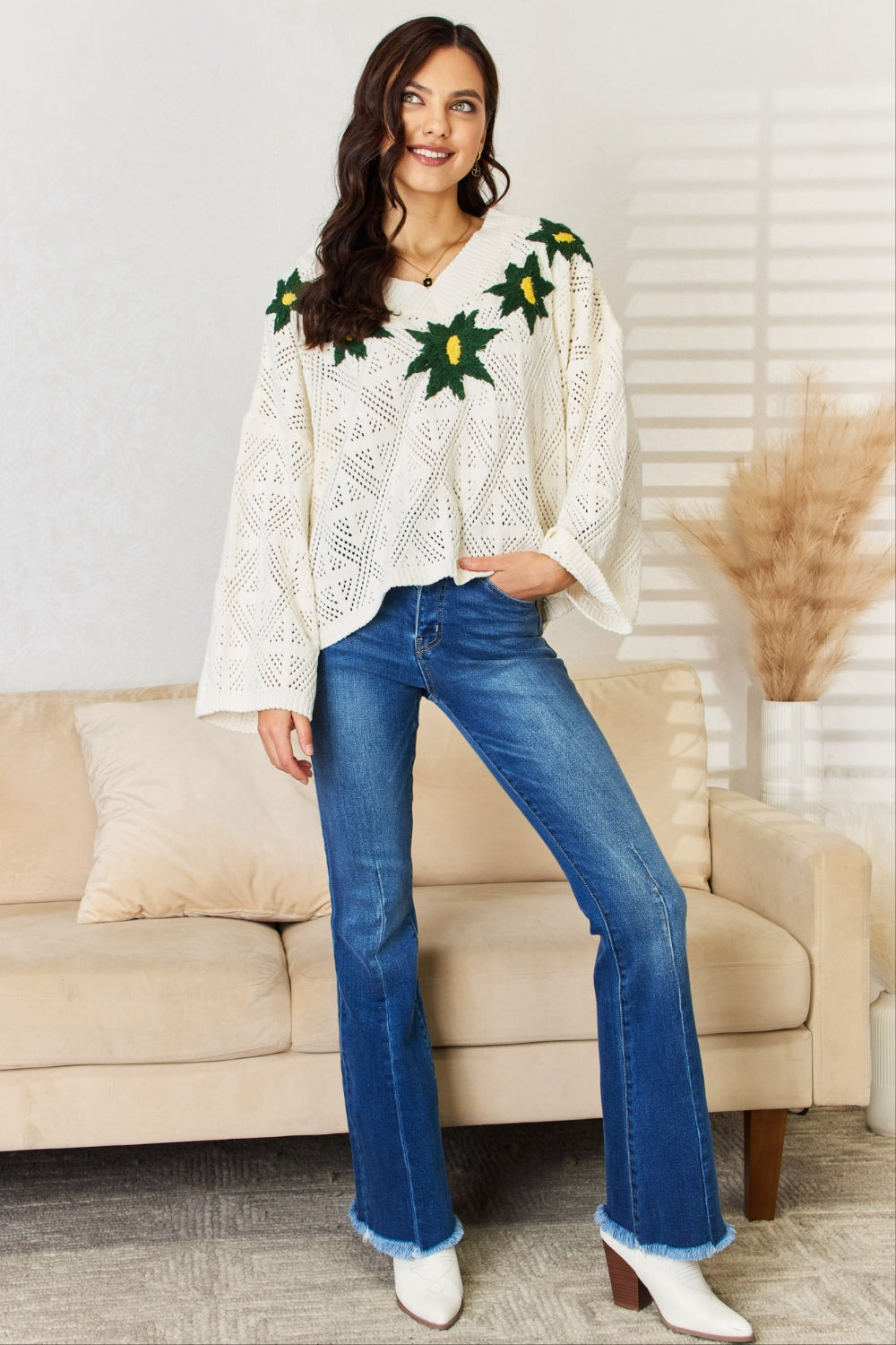 A woman wearing the POL Floral Embroidered Pattern V-Neck Sweater in creamy chenille paired with blue jeans, standing indoors.