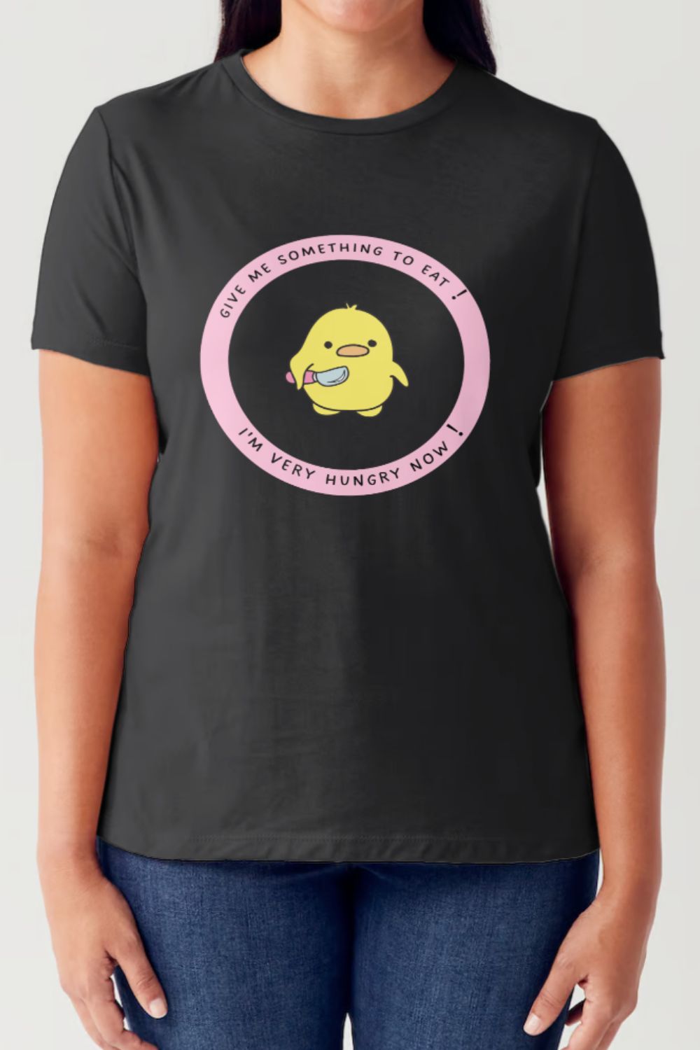 A person wearing the Simply Love Full Size Cute Graphic Short Sleeve Tubular T-Shirt, made of ringspun combed cotton and featuring a cartoon yellow bird in the center holding a fork and knife, surrounded by the text "Give me something to eat! I'm very hungry now!" in a pink circle. It's an ideal piece for any casual wardrobe.