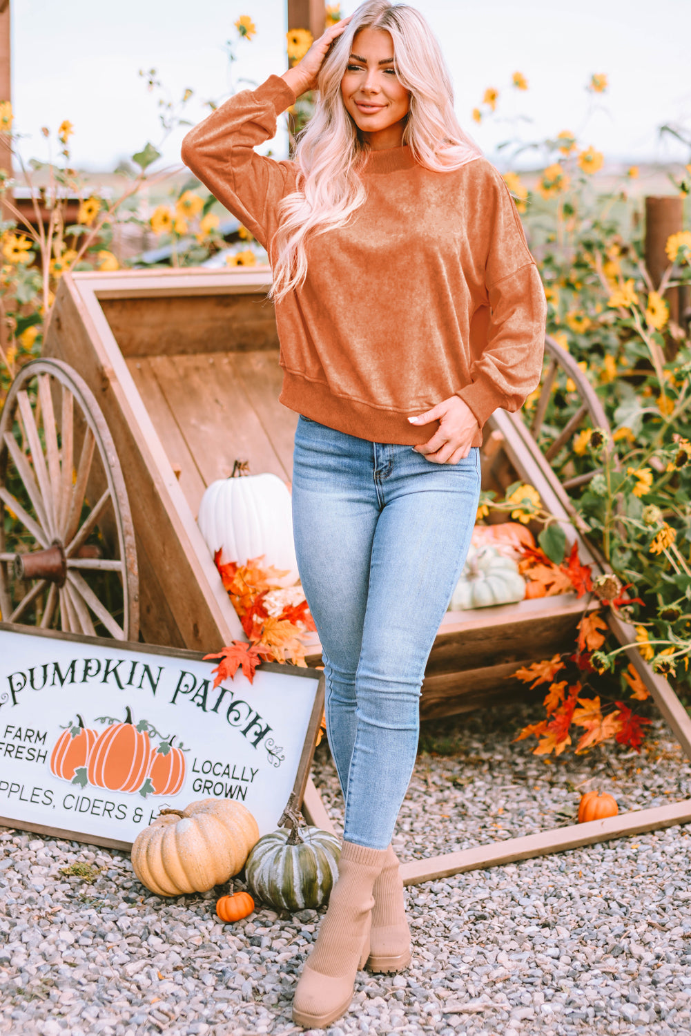 A person with long blonde hair wearing an Orange Drop Shoulder Crew Neck Pullover Sweatshirt and blue jeans stands with their back to the camera in a sunflower field.