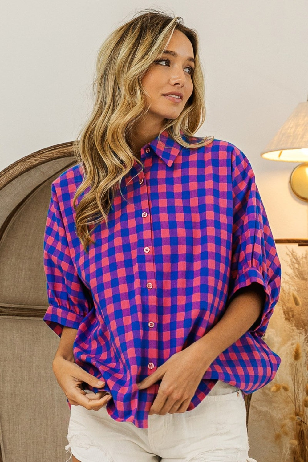 Person wearing a BiBi Plaid Button Up Dolman Sleeve Shirt in blue and pink with white shorts, standing in front of a wooden chair.