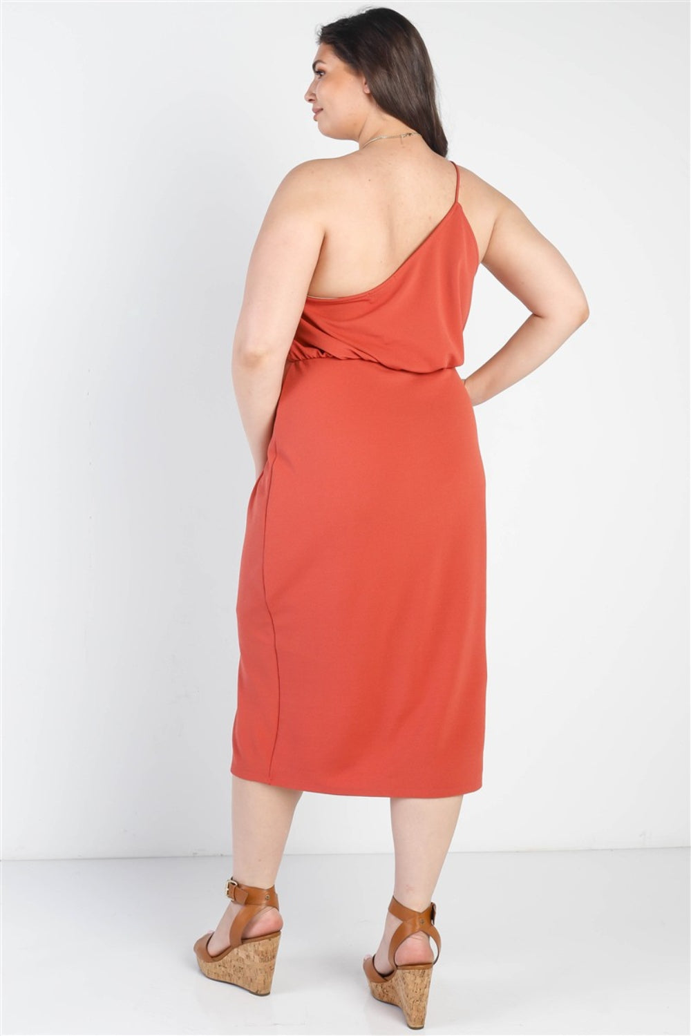 A woman in the Gilli Full Size Slit One Shoulder Sleeveless Dress, a rust-colored midi dress with slit detail, paired with tan high-heel sandals stands against a white background.