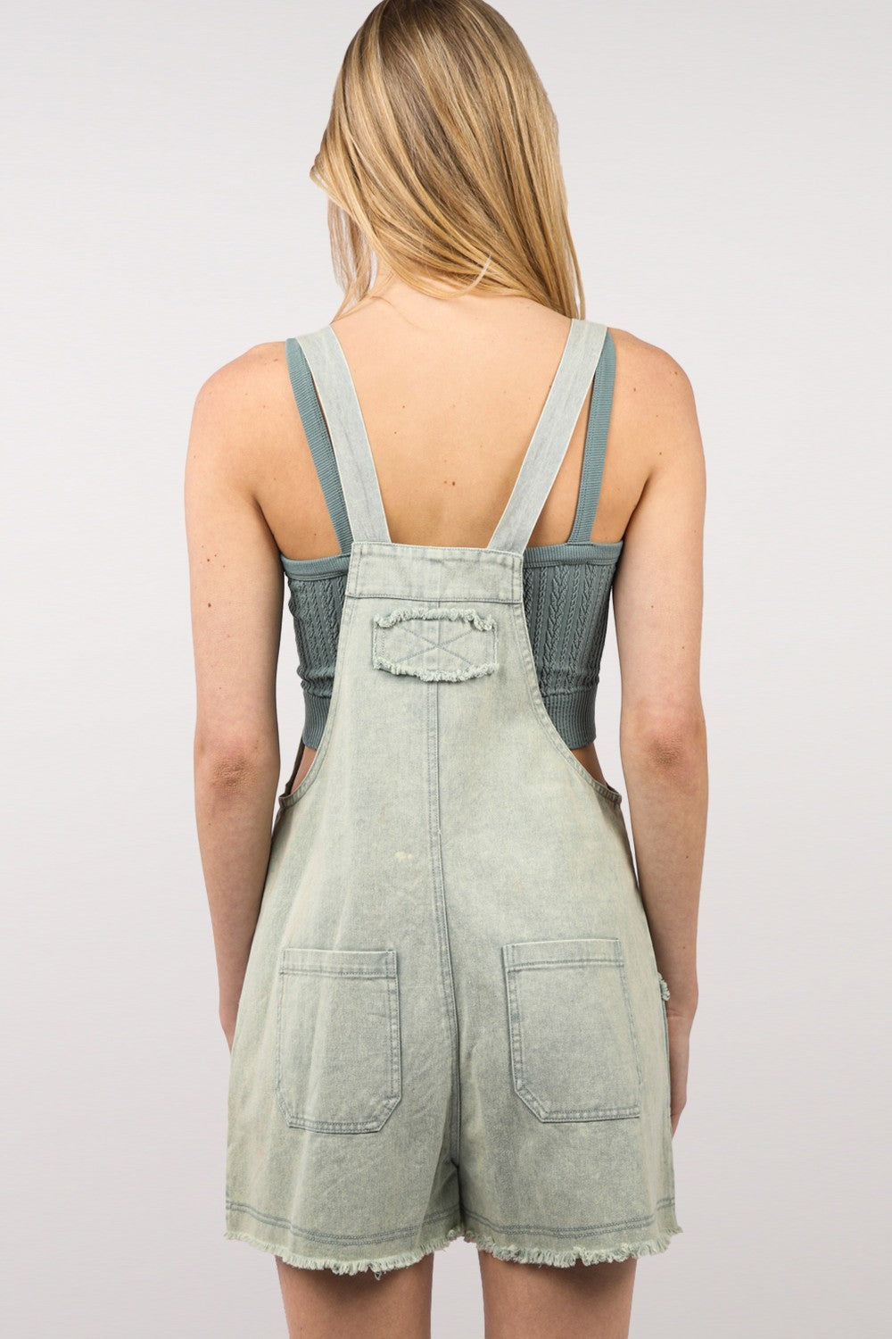 A young woman with shoulder-length hair wearing a green knit top and the VERY J Washed Frayed Hem Denim Overall stands against a plain background, effortlessly blending vintage fashion with a modern twist.