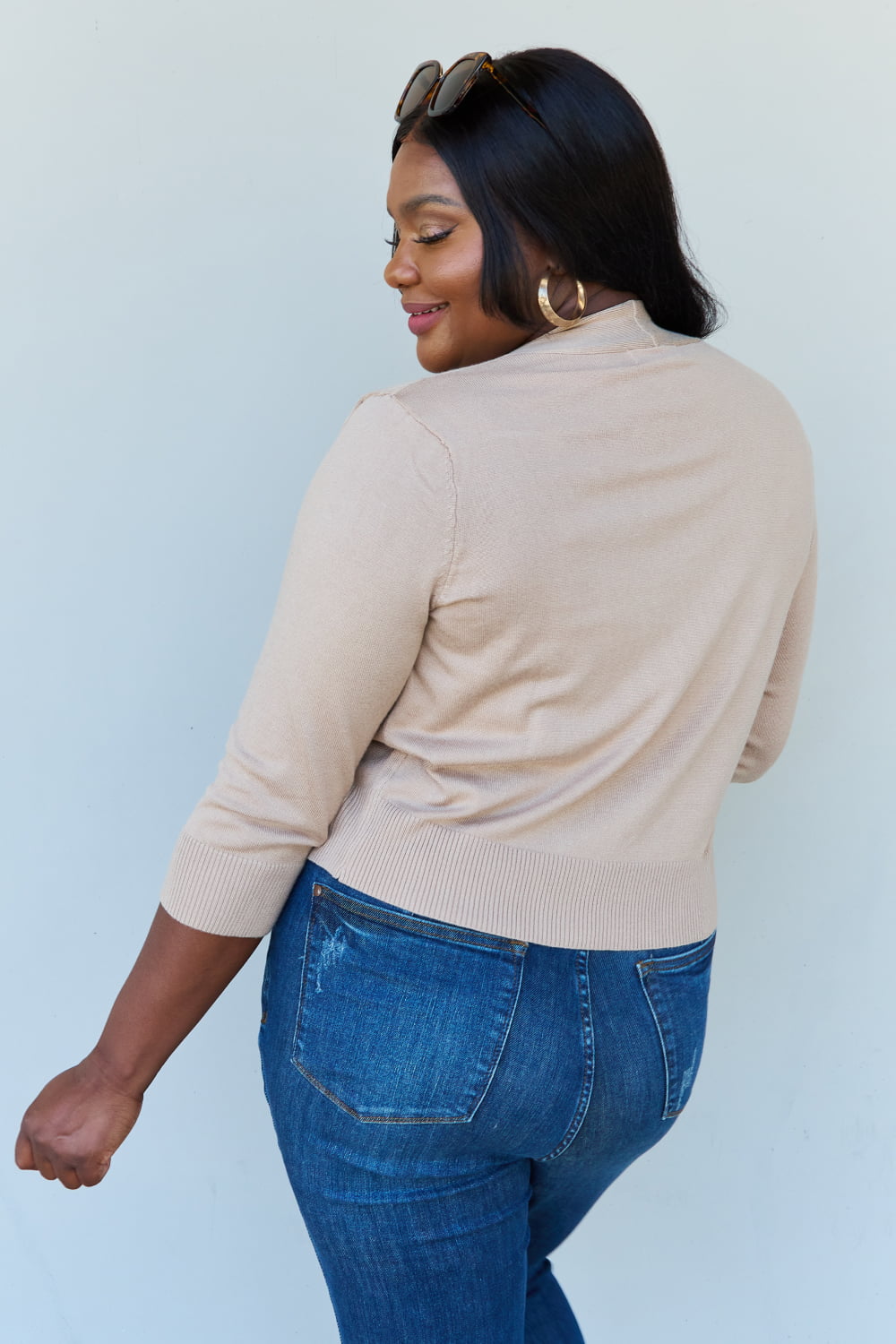 Woman with long dark hair wearing the versatile Doublju My Favorite Full Size 3/4 Sleeve Cropped Cardigan in Khaki over a white top and blue jeans, standing against a plain background.