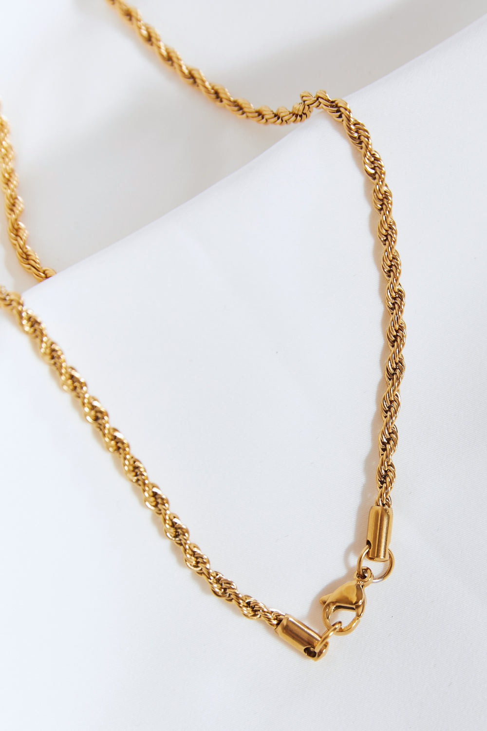 A Brass Lightning Pendant Necklace, featuring a gold twisted chain and a lightning bolt-shaped pendant encrusted with small cubic zirconia stones, displayed on a light blue background.