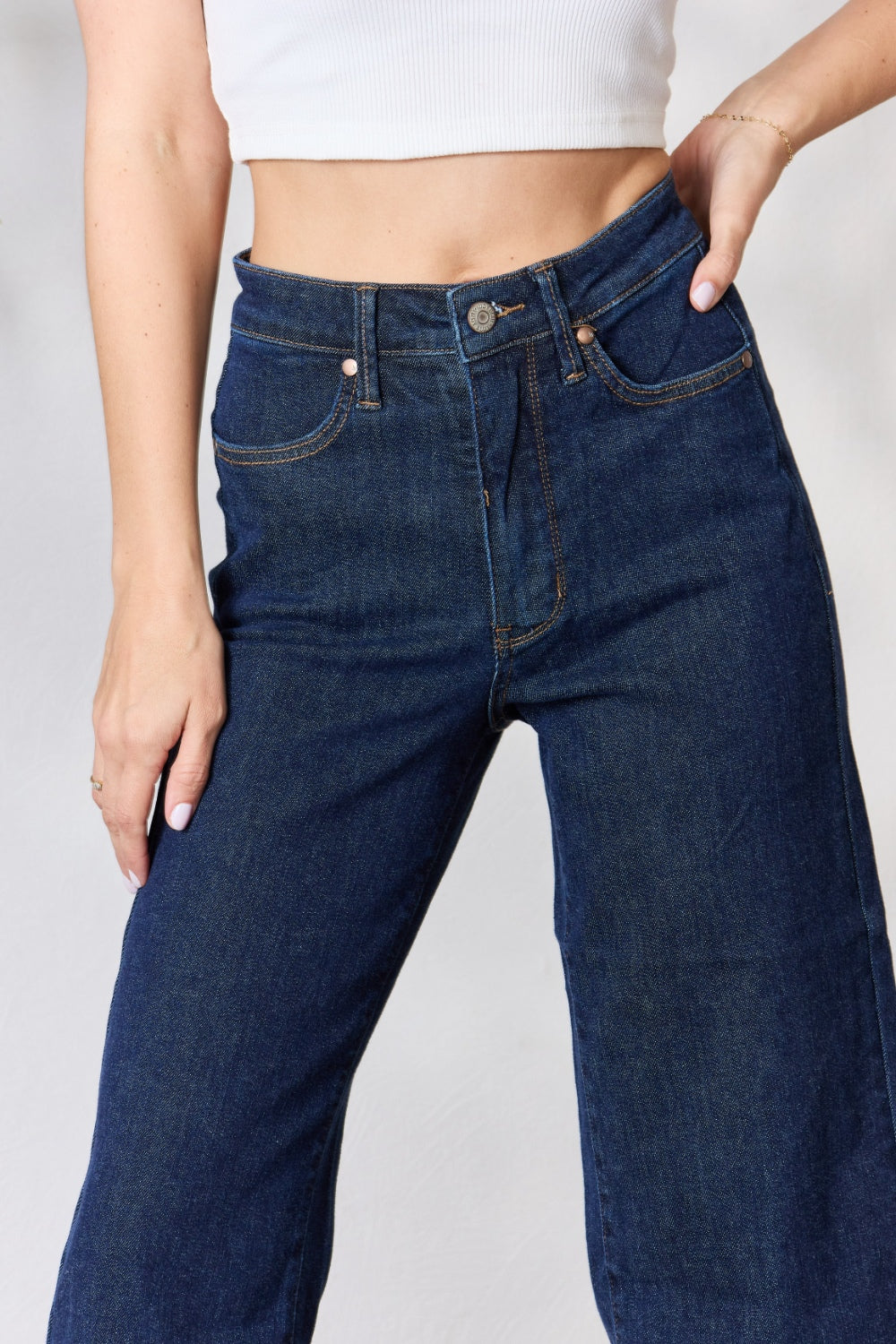 A person wearing the Judy Blue Full Size High Waist Cropped Wide Leg Jeans, which are renowned for their tummy control design, and nude block heel sandals stands near a potted plant.