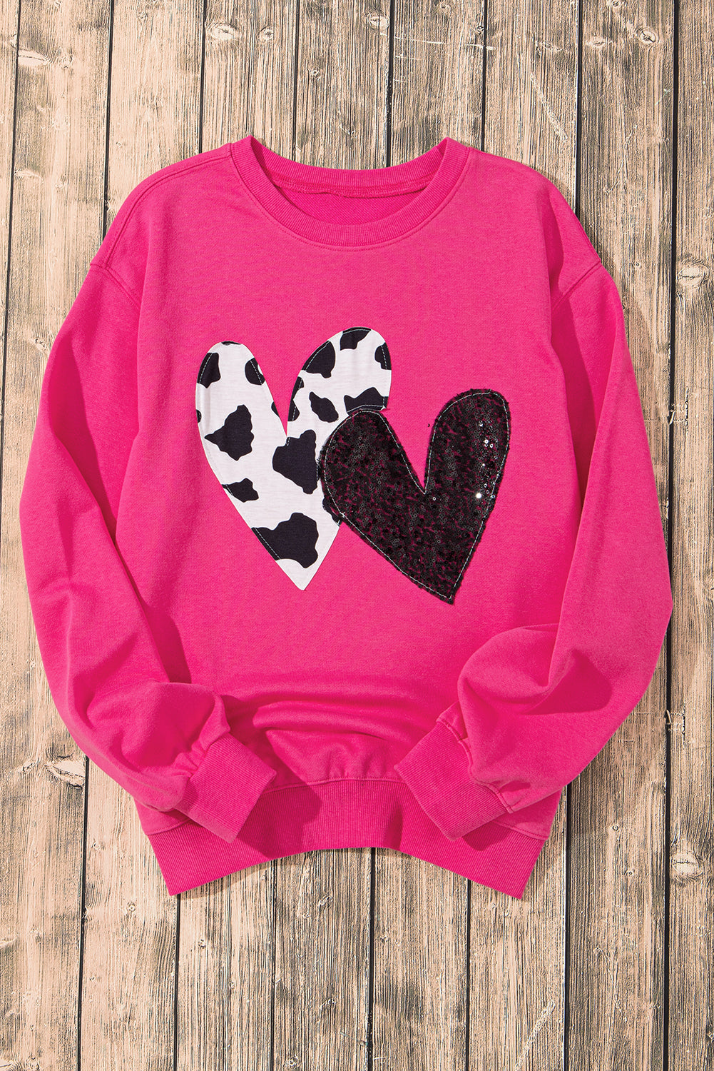 A person with long blonde hair, seen from the back, is wearing a Strawberry Pink Cow & Sequin Double Heart Patch Graphic Sweatshirt and light blue jeans.