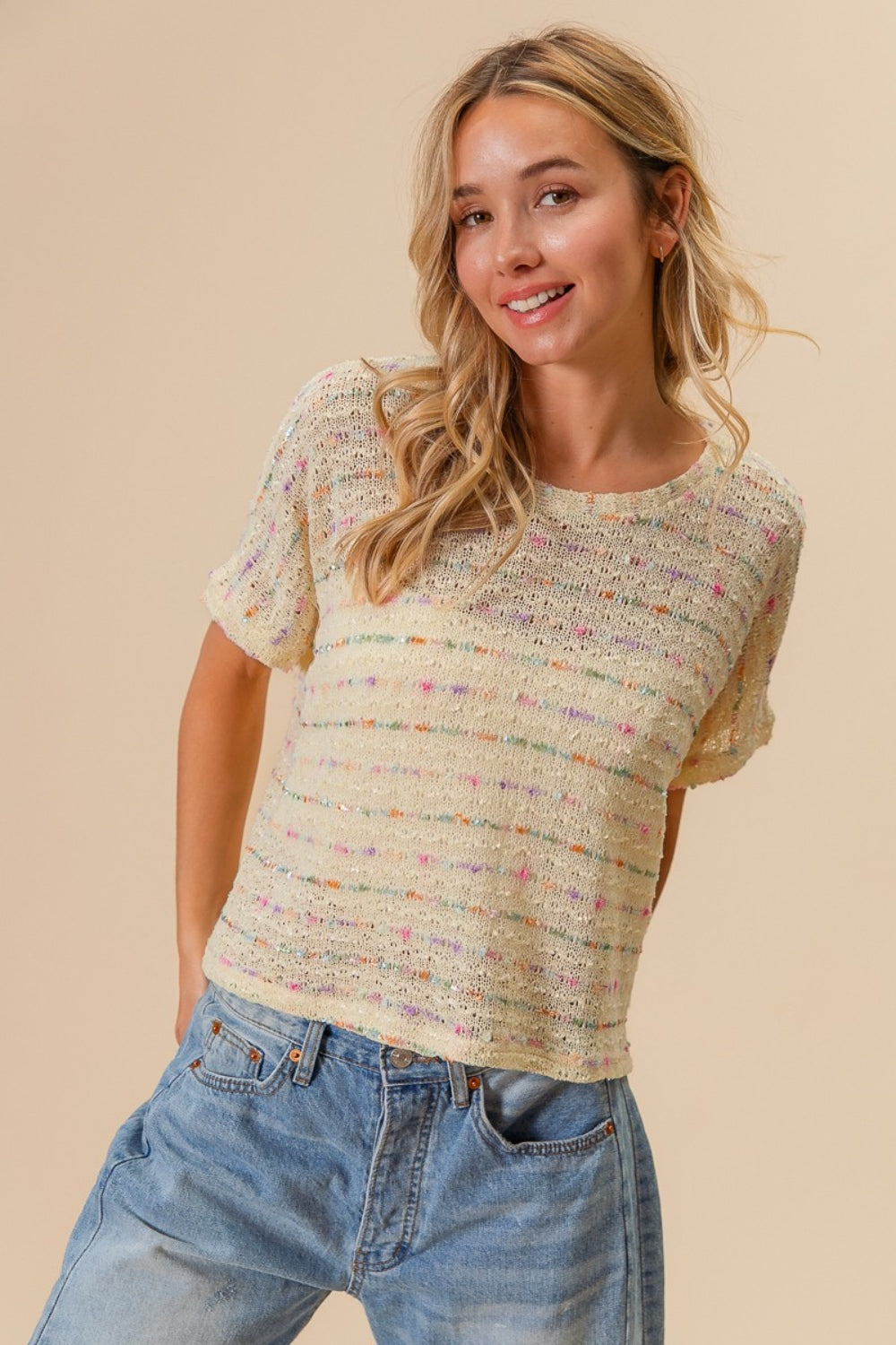 A person with long hair wearing the BiBi Striped Popcorn Knit Top and jeans stands against a neutral background, smiling.