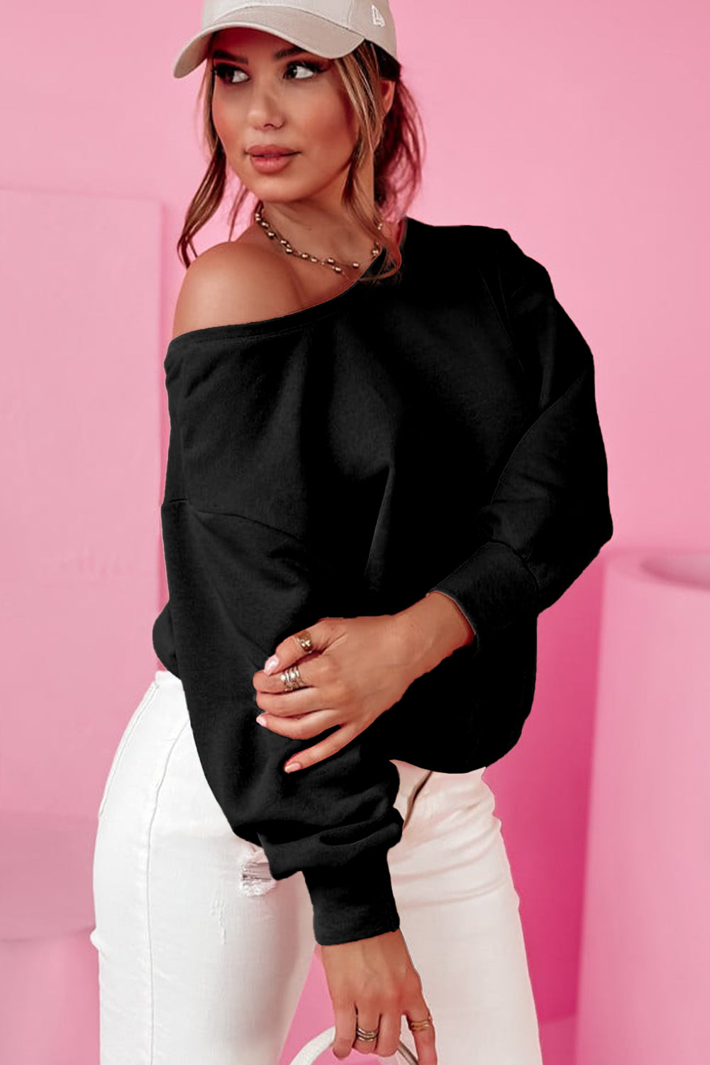 A person wearing a Black Bowknot Dewback Round Neck Sweatshirt, white pants, and a light-colored cap stands against a pink background. The individual has one hand on their hip and is looking down.