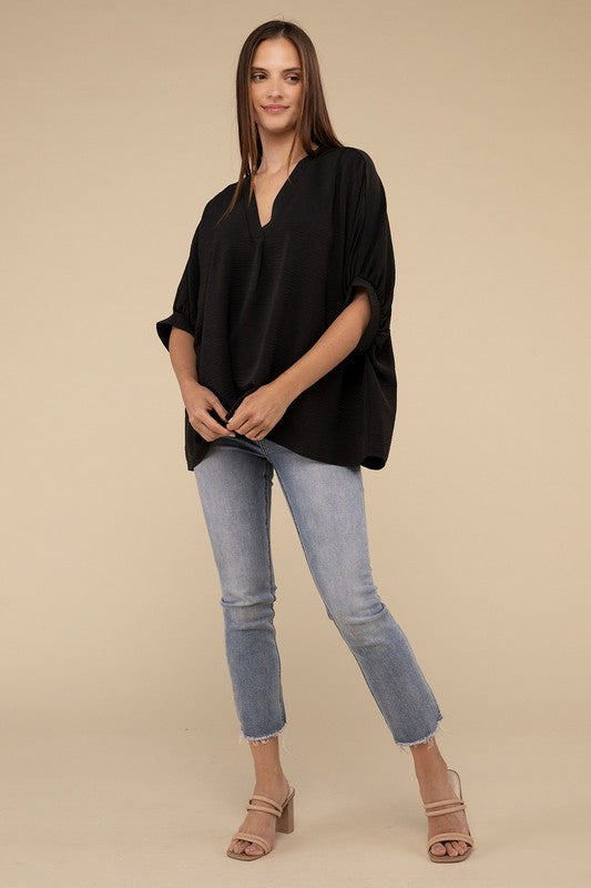 A woman in a Woven Airflow V-Neck Puff half sleeve top and blue jeans stands with her hand on her hip, looking to her right.