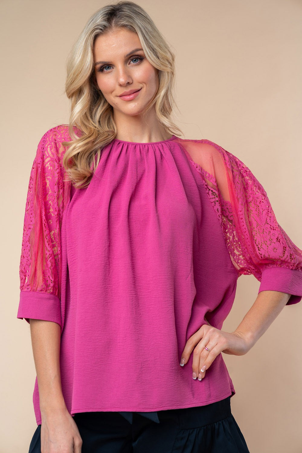 A person stands against a neutral background, wearing the White Birch round neck blouse with vibrant pink lace half sleeves.