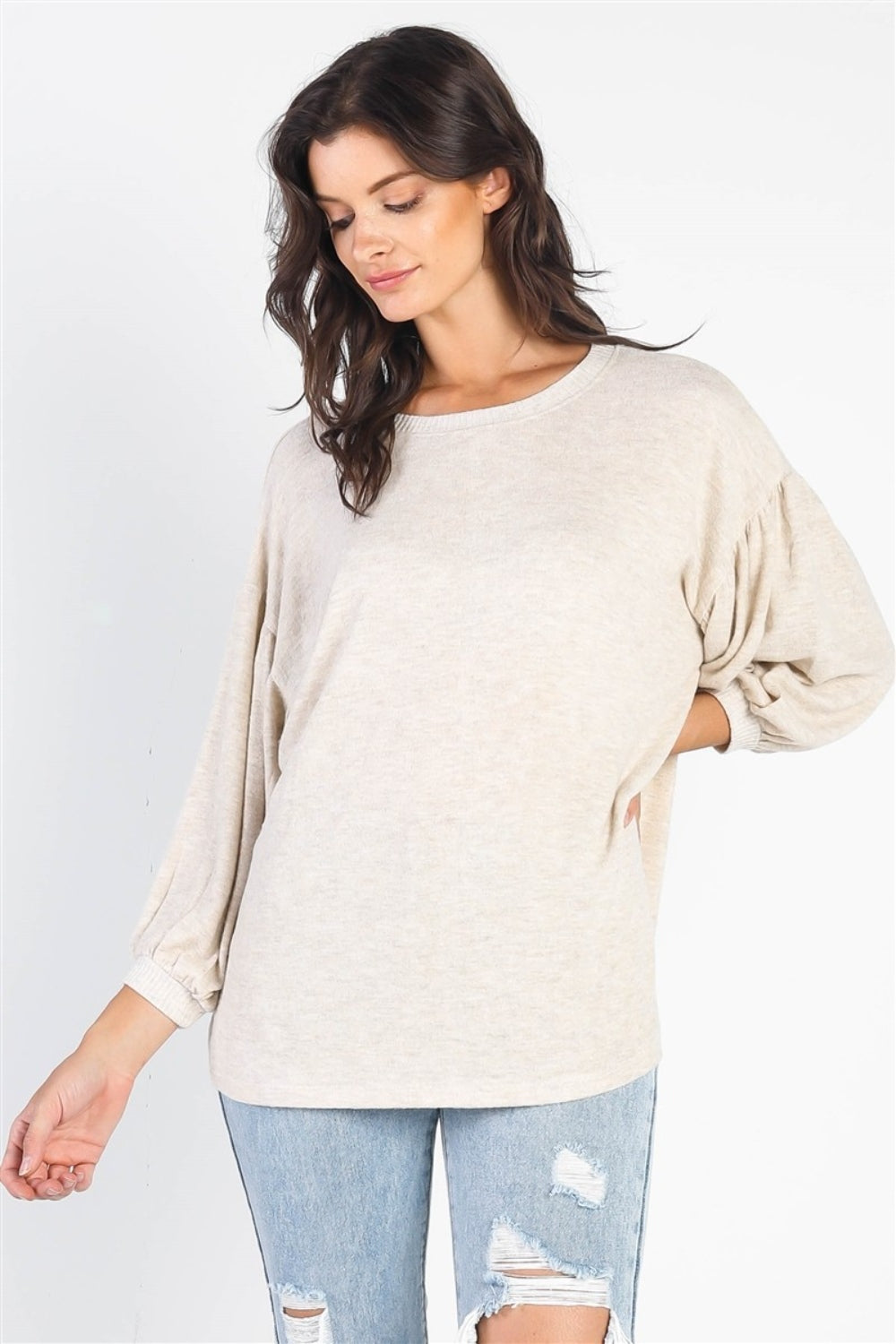 A person with long dark hair stands against a white background, smiling and raising one hand while wearing the trendy and stylish Cherish Apparel Drop Shoulder Puff Sleeve Top in burgundy paired with light blue jeans.