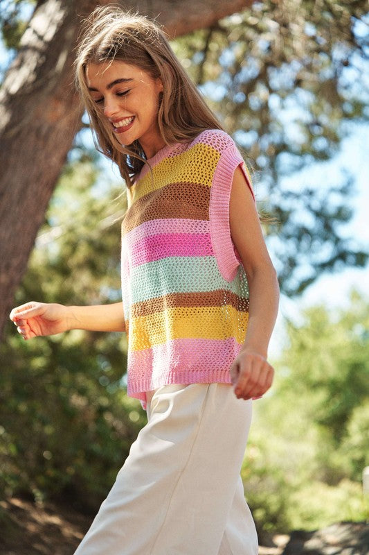 A woman outdoors wearing a Crochet Multi Striped Pullover Knit Sweater Vest and white pants, with her arms raised and eyes closed.