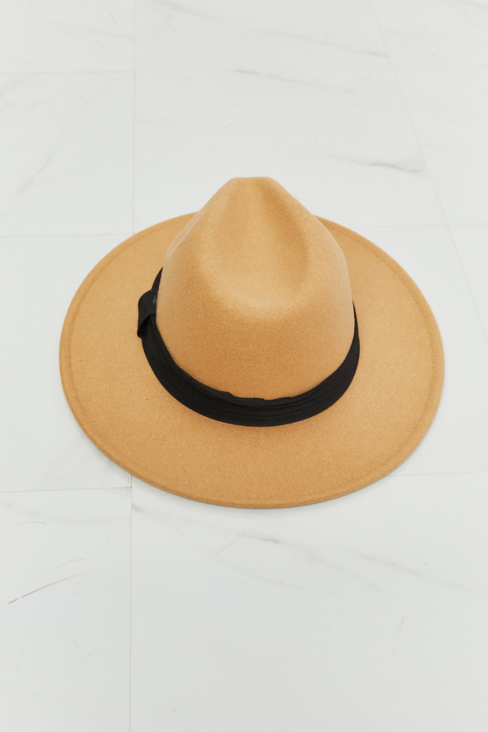 A woman in a white dress with adjustable straps, paired with the dark tan Fame You Got It Fedora Hat featuring a black band, looks over her shoulder and smiles.