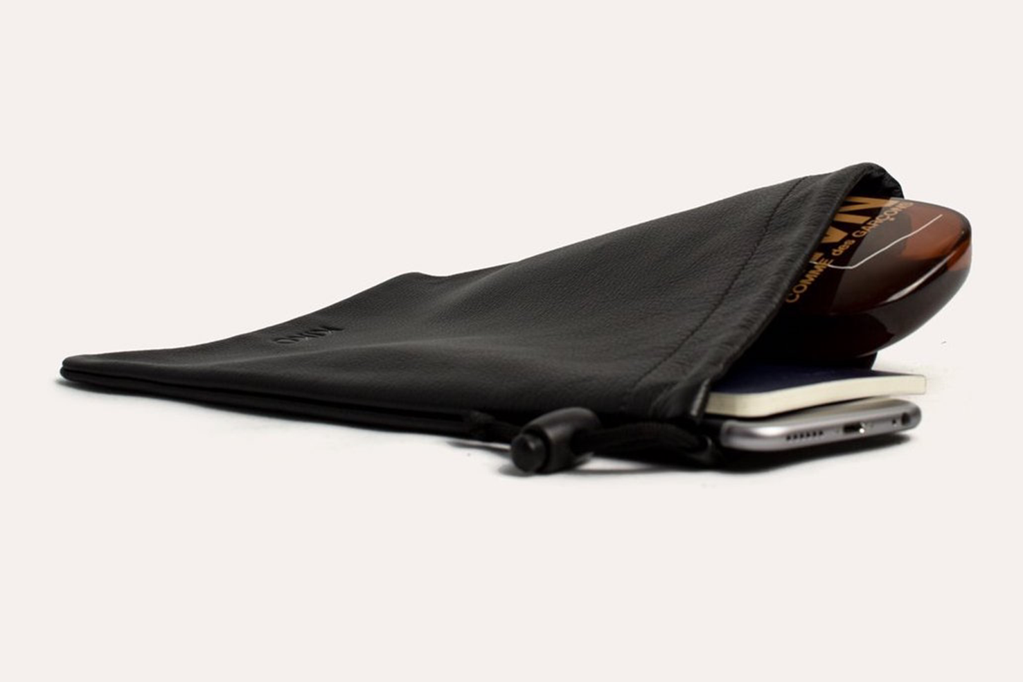 A sophisticated black Accessory Pouch, fashioned from high-quality cowhide leather, partially open to display a smartphone, a chocolate bar, and an additional small item inside. The adjustable closure provides a secure fit for all your essentials.