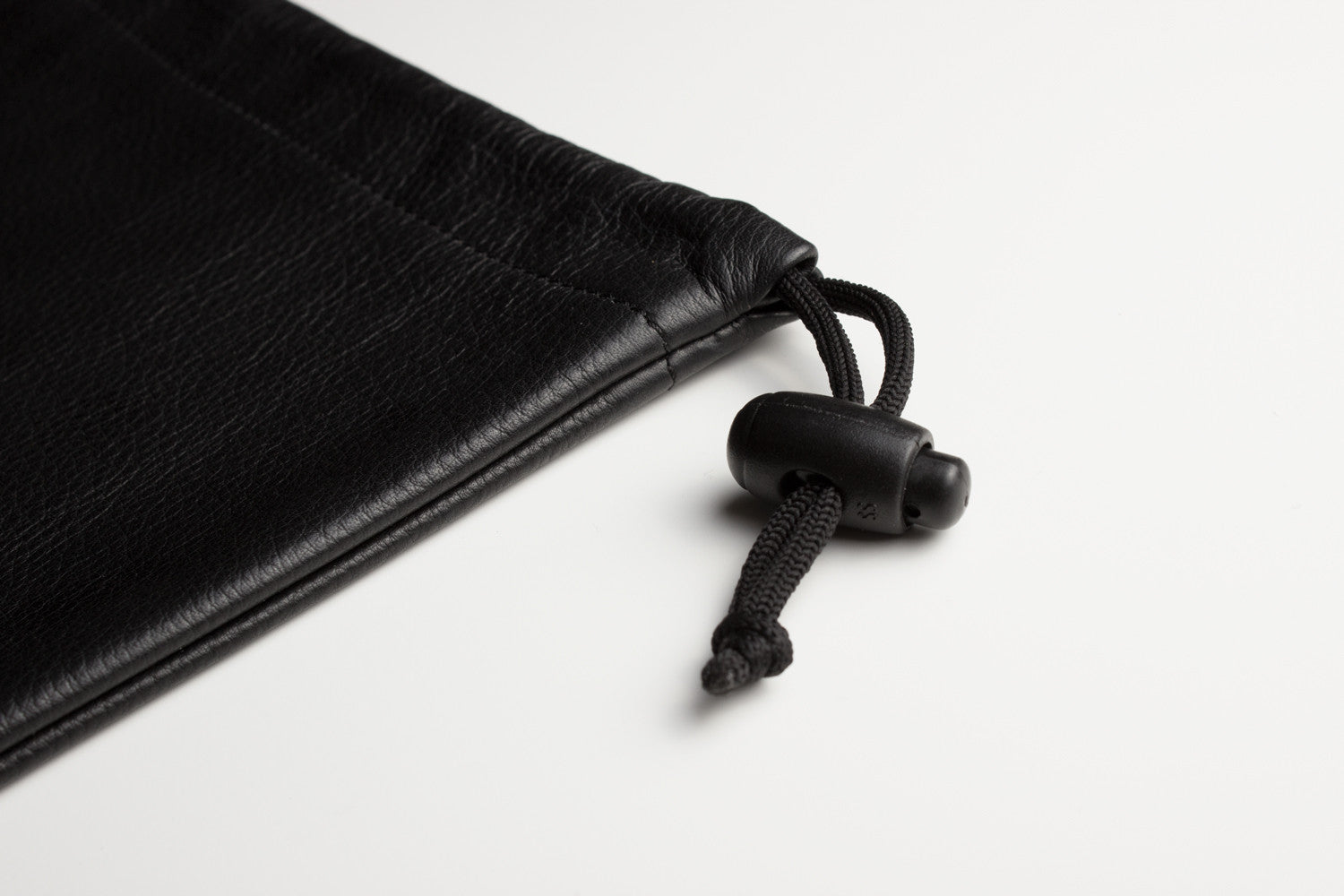 A sophisticated black Accessory Pouch, fashioned from high-quality cowhide leather, partially open to display a smartphone, a chocolate bar, and an additional small item inside. The adjustable closure provides a secure fit for all your essentials.