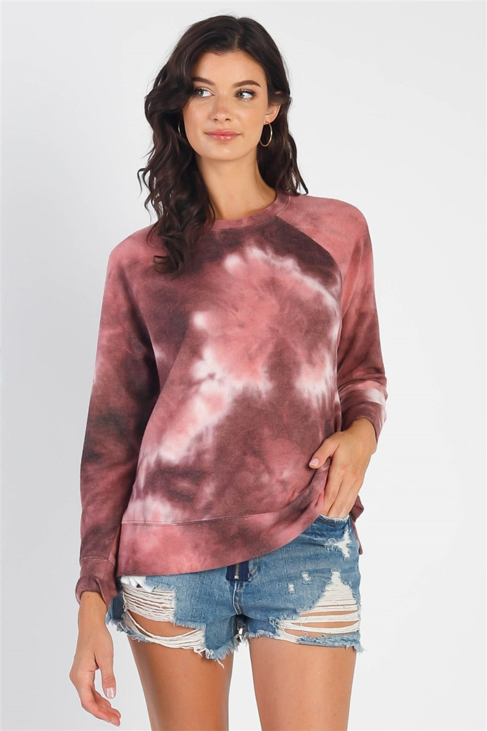 A person wearing the Cherish Apparel Tie-Dye Round Neck Long Sleeve Sweatshirt and distressed denim shorts stands against a plain background, showcasing effortless casual fashion.