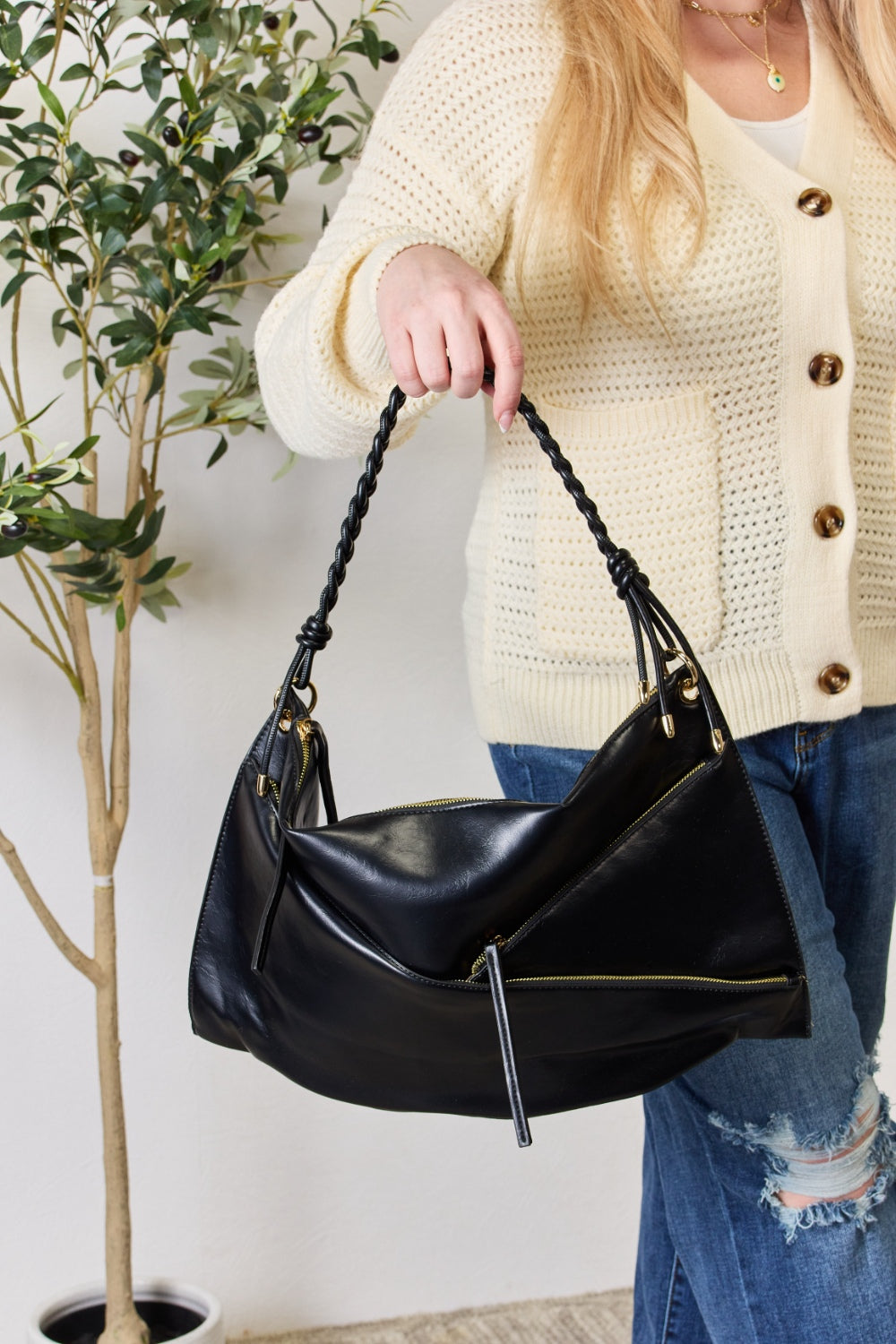 A person in a cream sweater holds a medium-size SHOMICO Zipper Detail Shoulder Bag with gold metal zipper pockets.