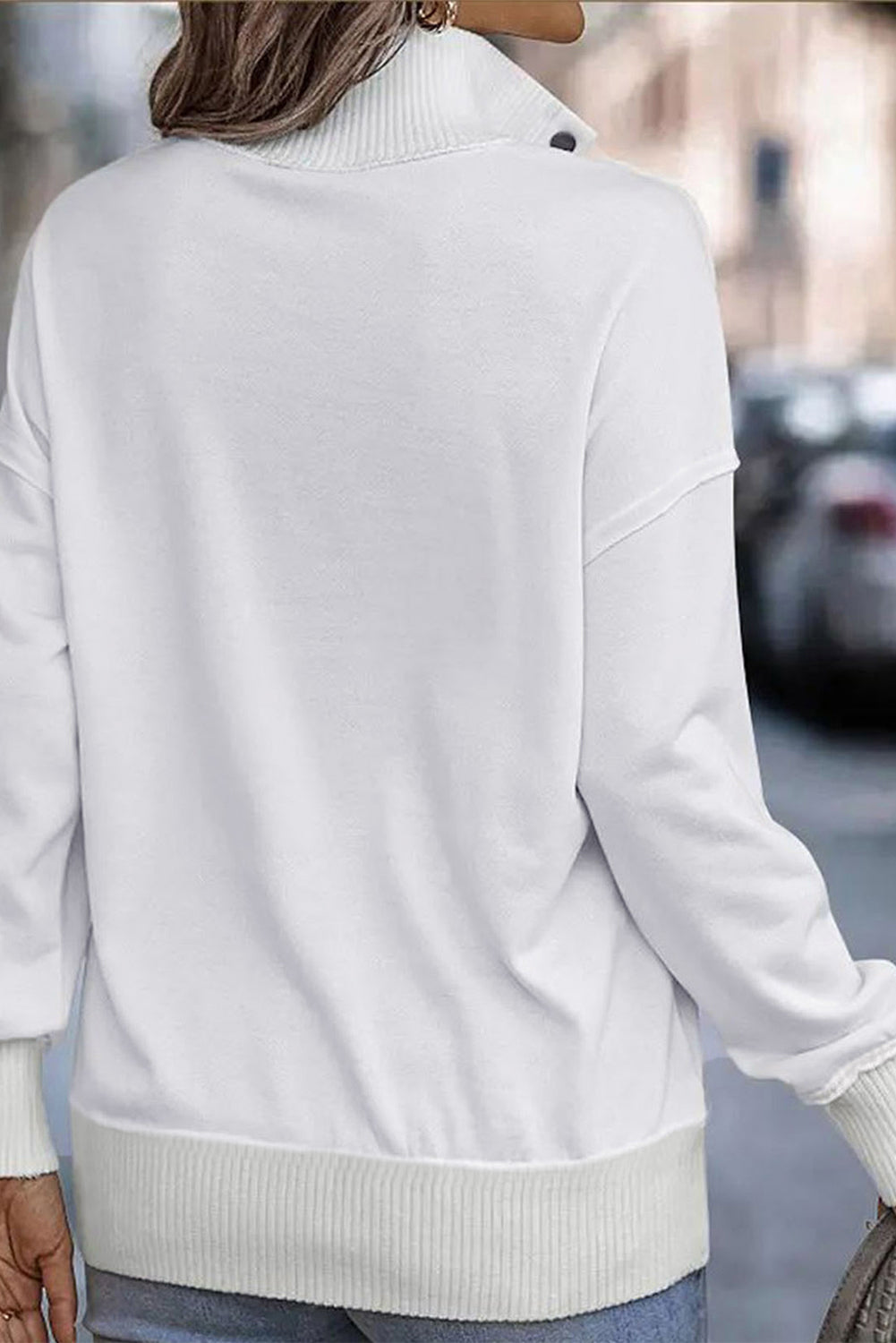 A woman with long hair wearing a White Ribbed Hem Snap Button Neckline Sweatshirt with Pocket is seen from behind, standing against a plain background, embodying a casual look.